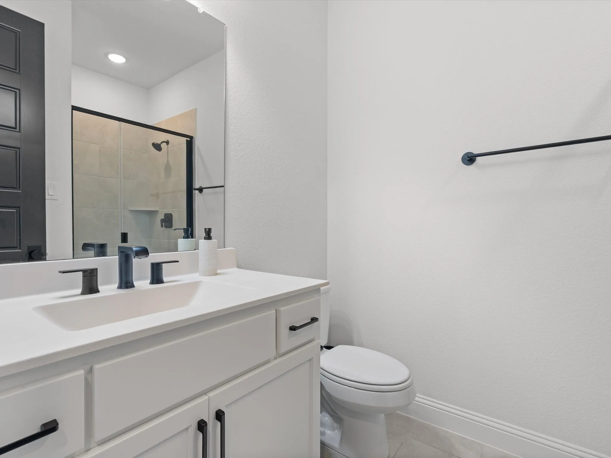 White vanity with black hardware, integrated rectangular sink, matte black two-handle faucet, and frameless mirror