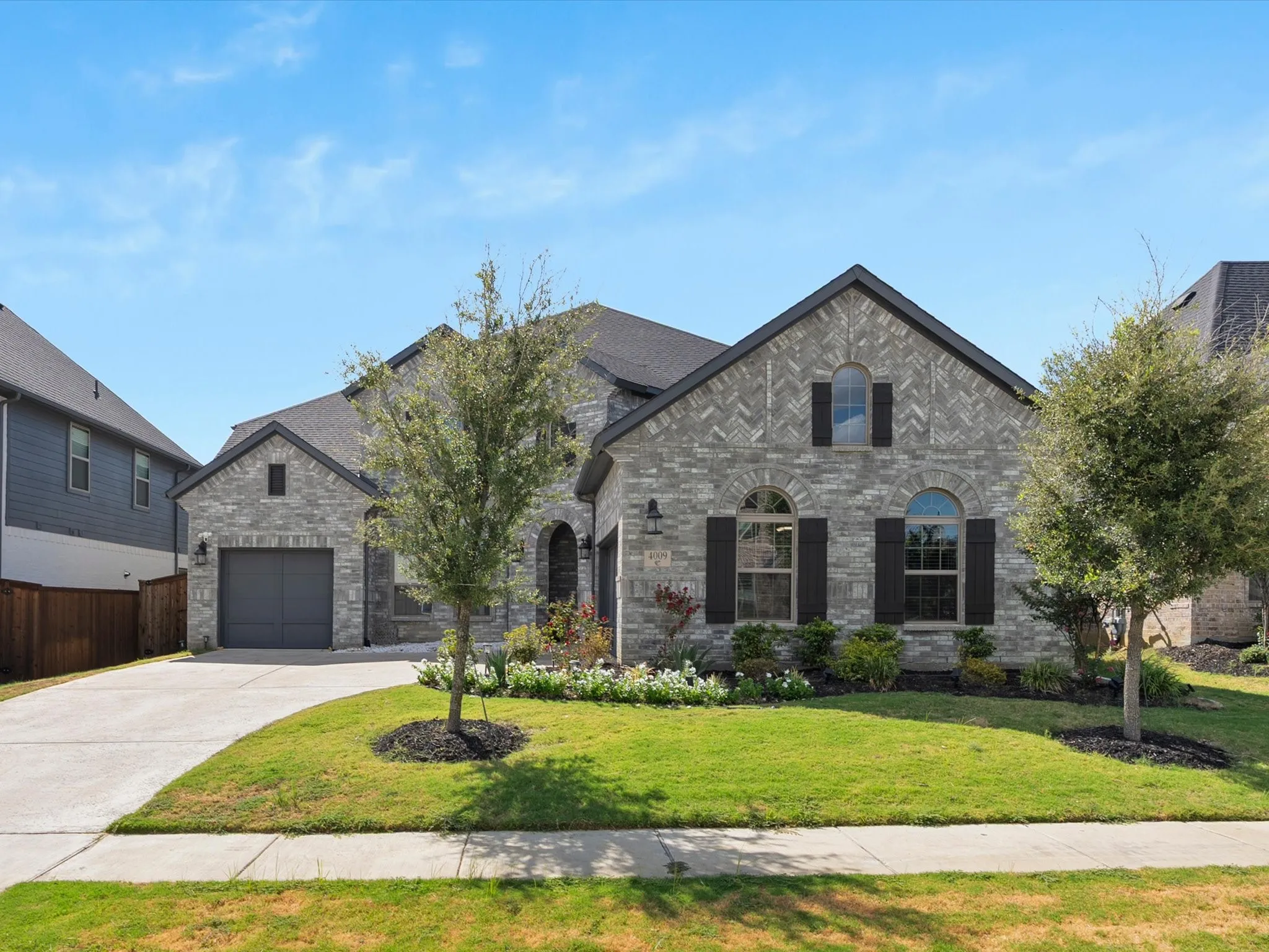 Stone facade, arched windows, dark shutters, concrete driveway, and a well-maintained lawn