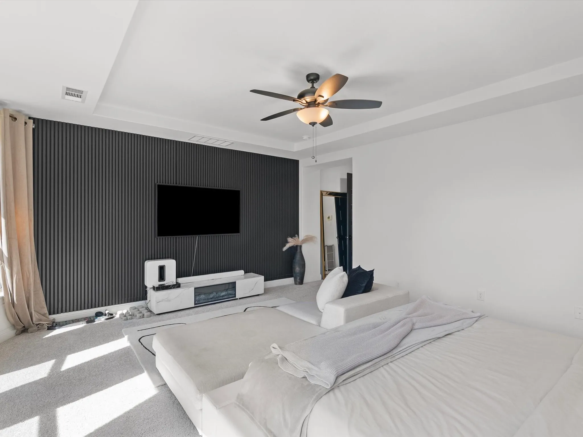 Textured dark accent wall, recessed ceiling, ceiling fan with integrated lighting, built-in electric fireplace, and plush carpeting