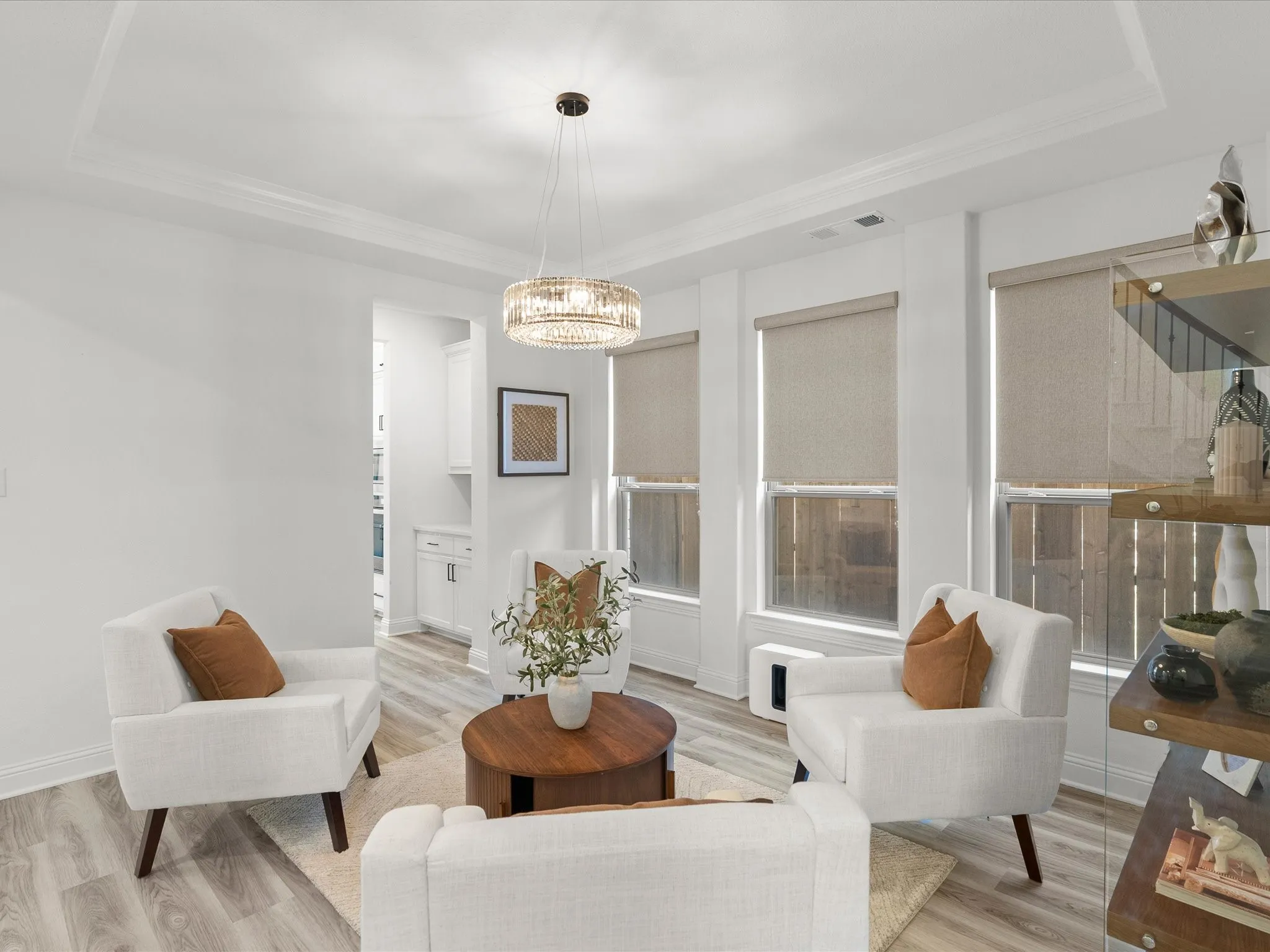 Tray ceiling with crown molding, contemporary chandelier, wood-finish flooring, and multiple windows with roller shades