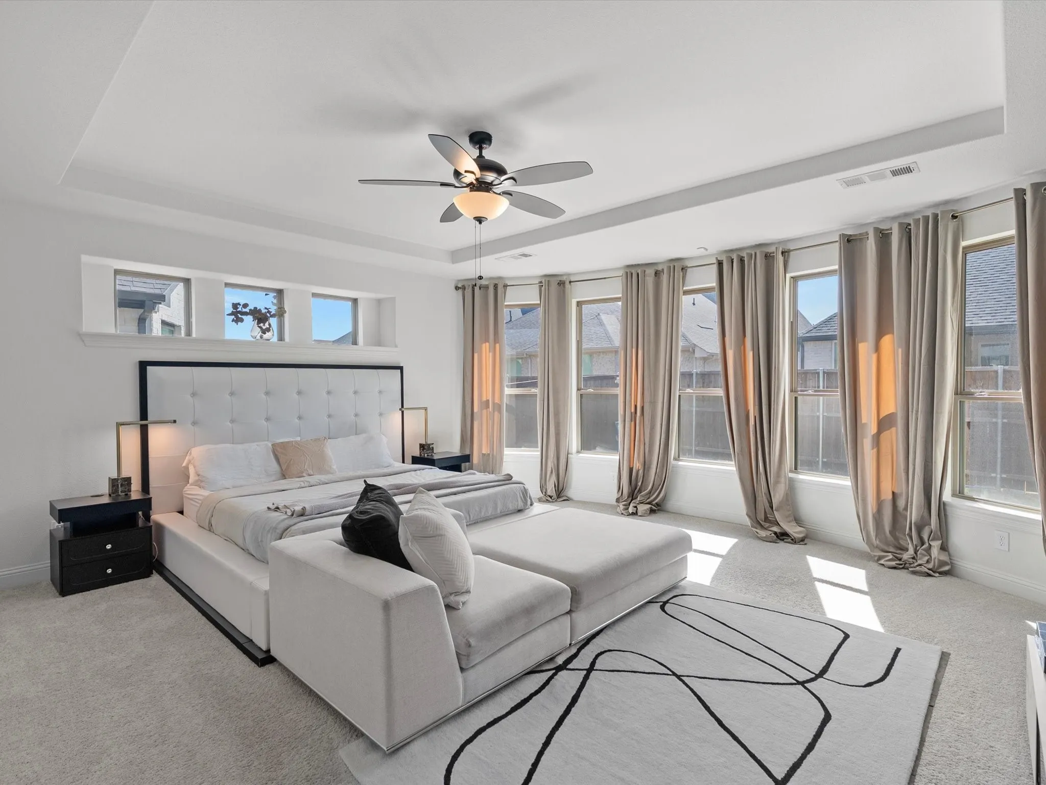 Recessed ceiling with an integrated ceiling fan, carpet flooring, a wall of tall windows, and three transom windows