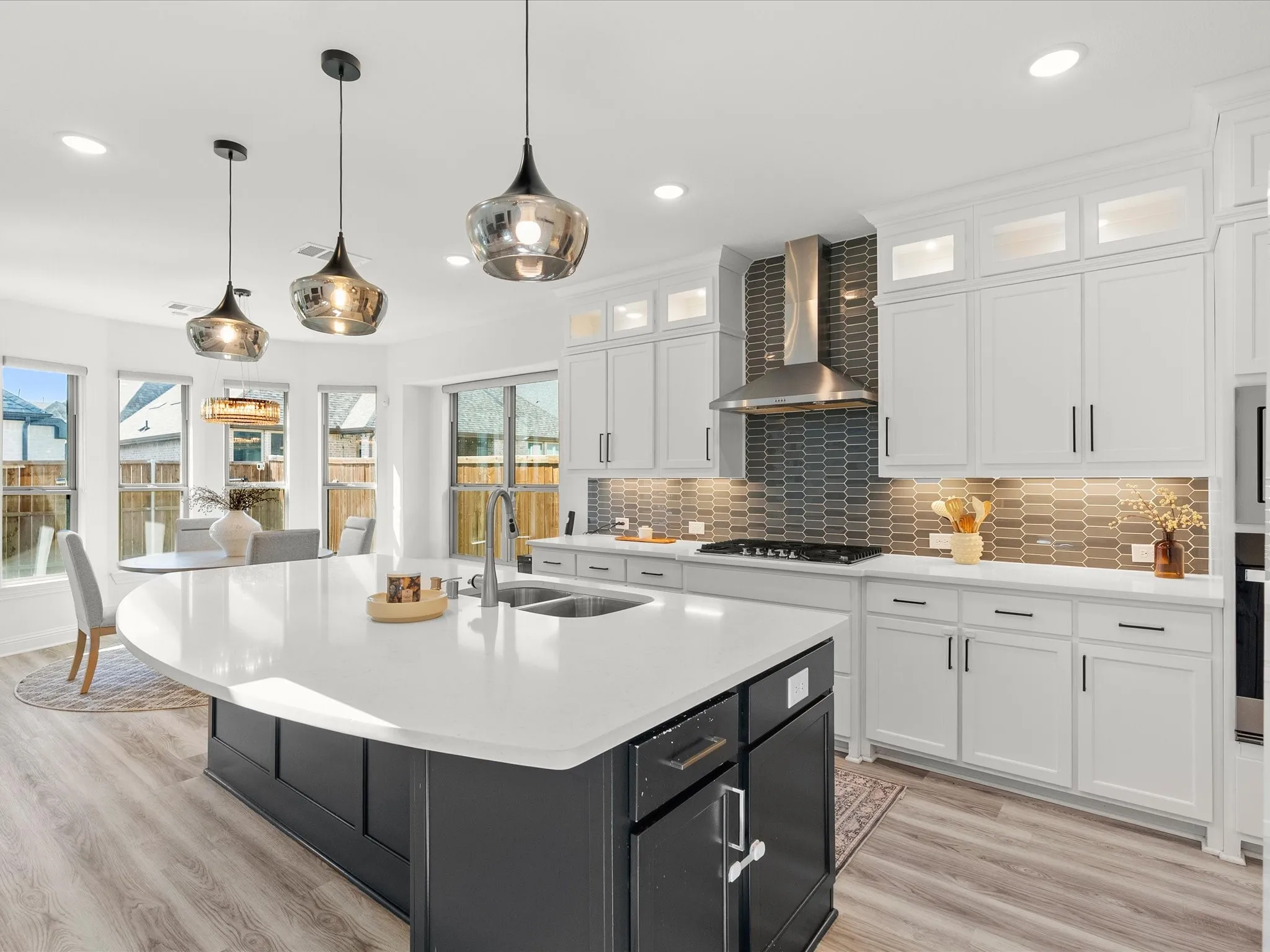 Modern kitchen featuring a large central island with seating, white shaker-style cabinetry, stainless steel appliances, and wood-finish flooring