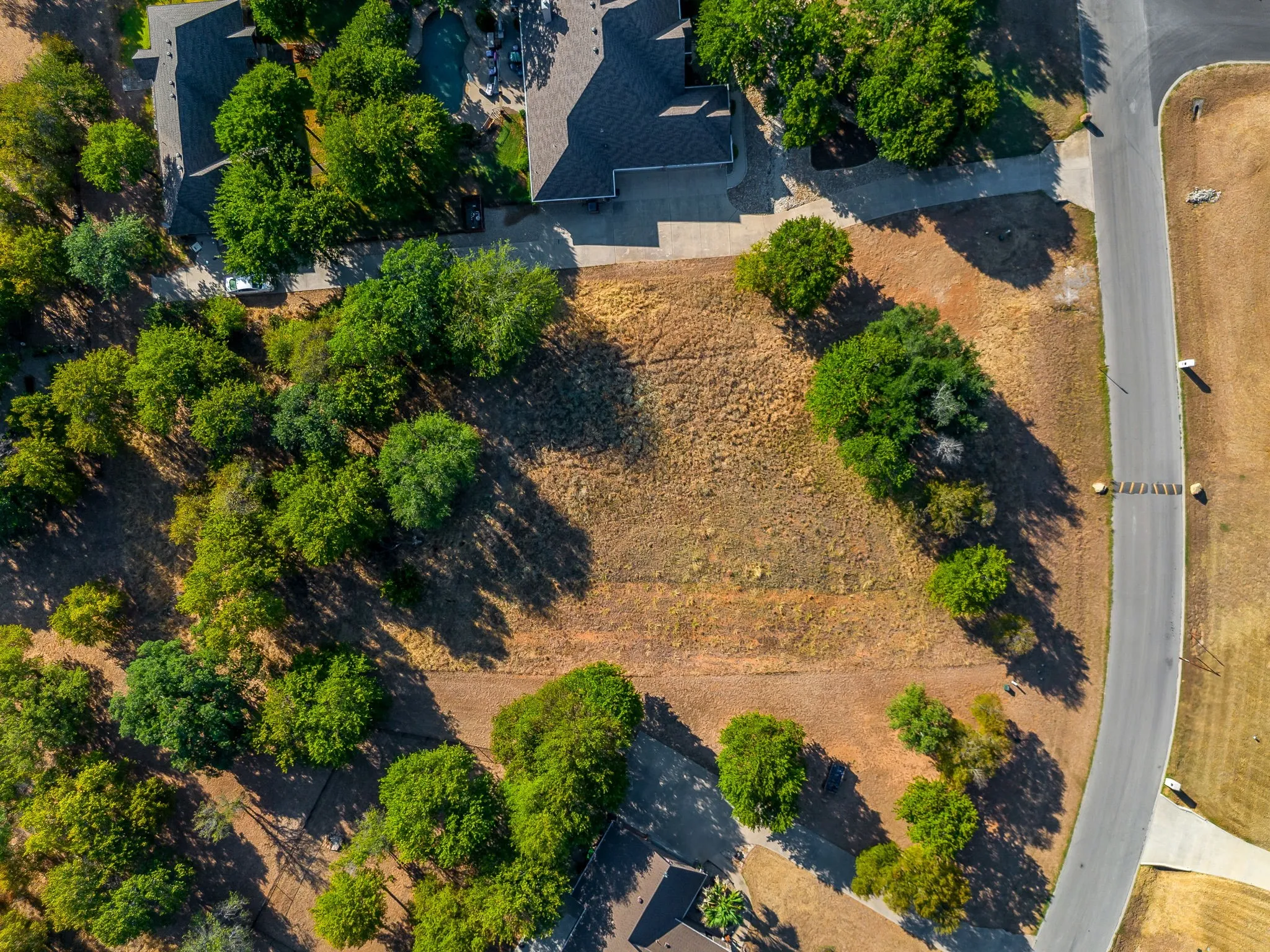 Expansive undeveloped lot with mature trees, established residential structures, and paved road access