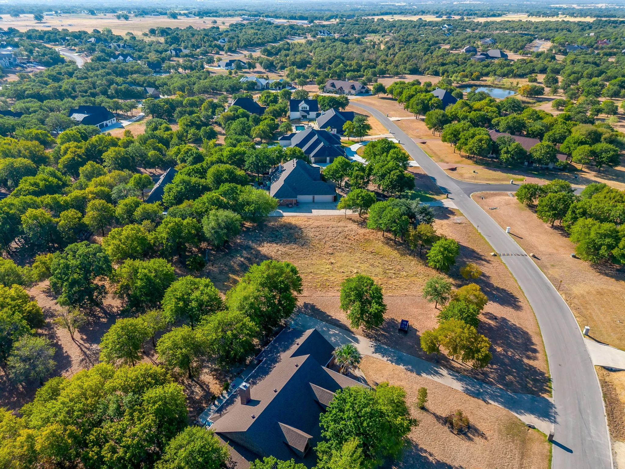 Expansive land parcel with surrounding mature trees and a paved street