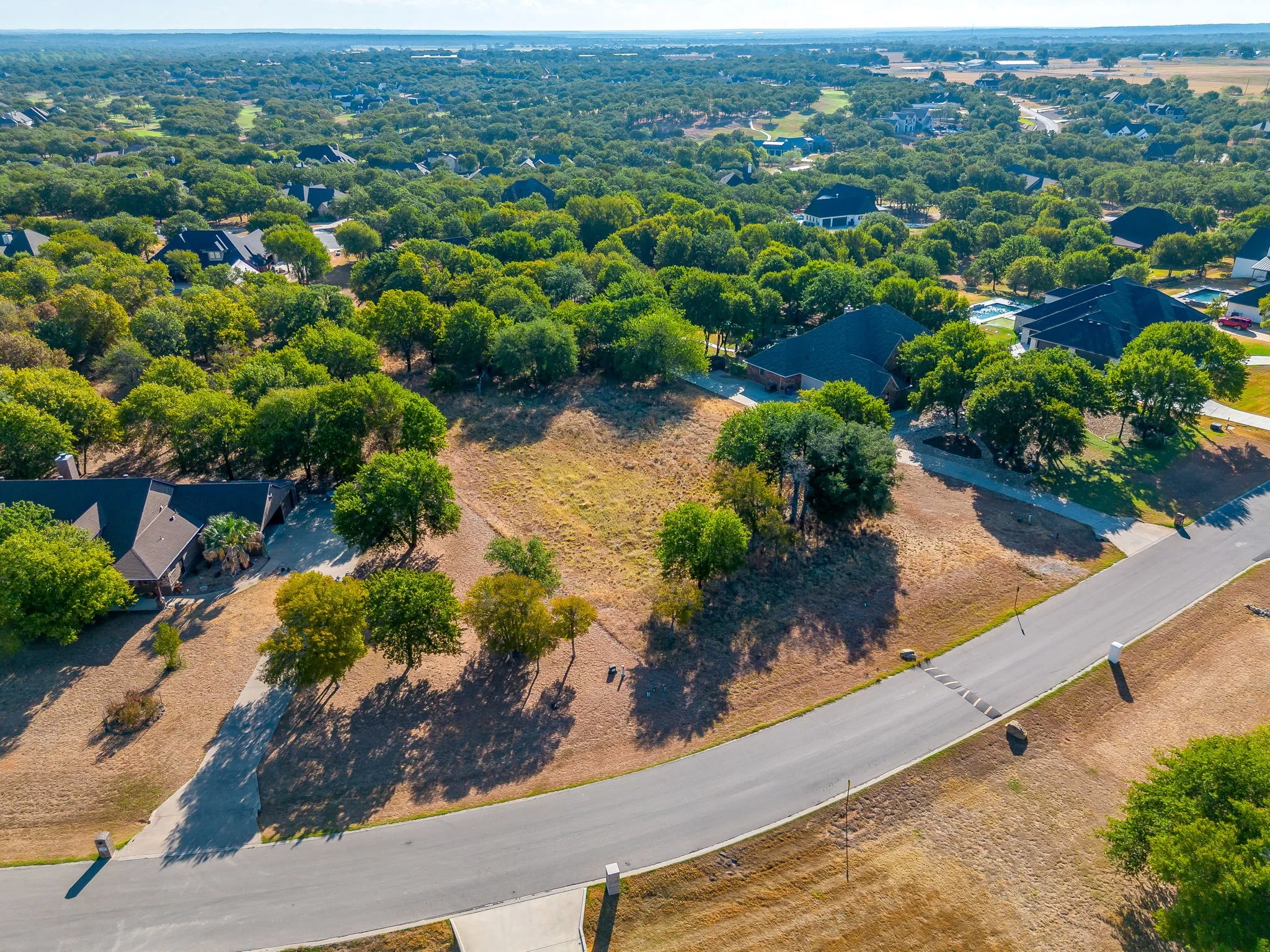 Expansive lot with mature trees, surrounded by residential properties, featuring a paved road