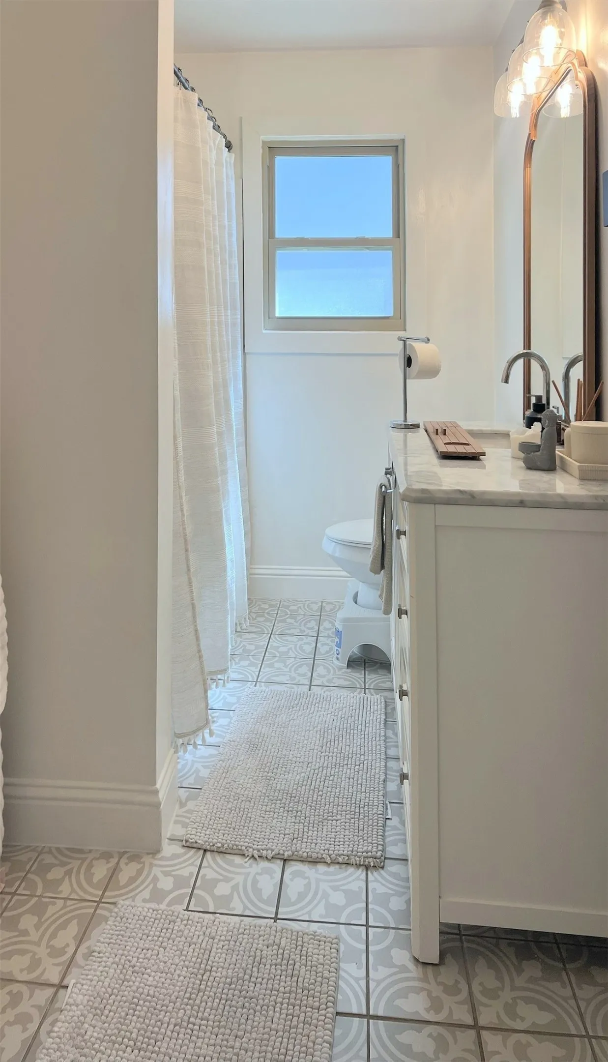 Bathroom featuring a white vanity with a light-toned countertop, patterned floor tiling, a single window, and a wall-mounted light fixture above a mirror