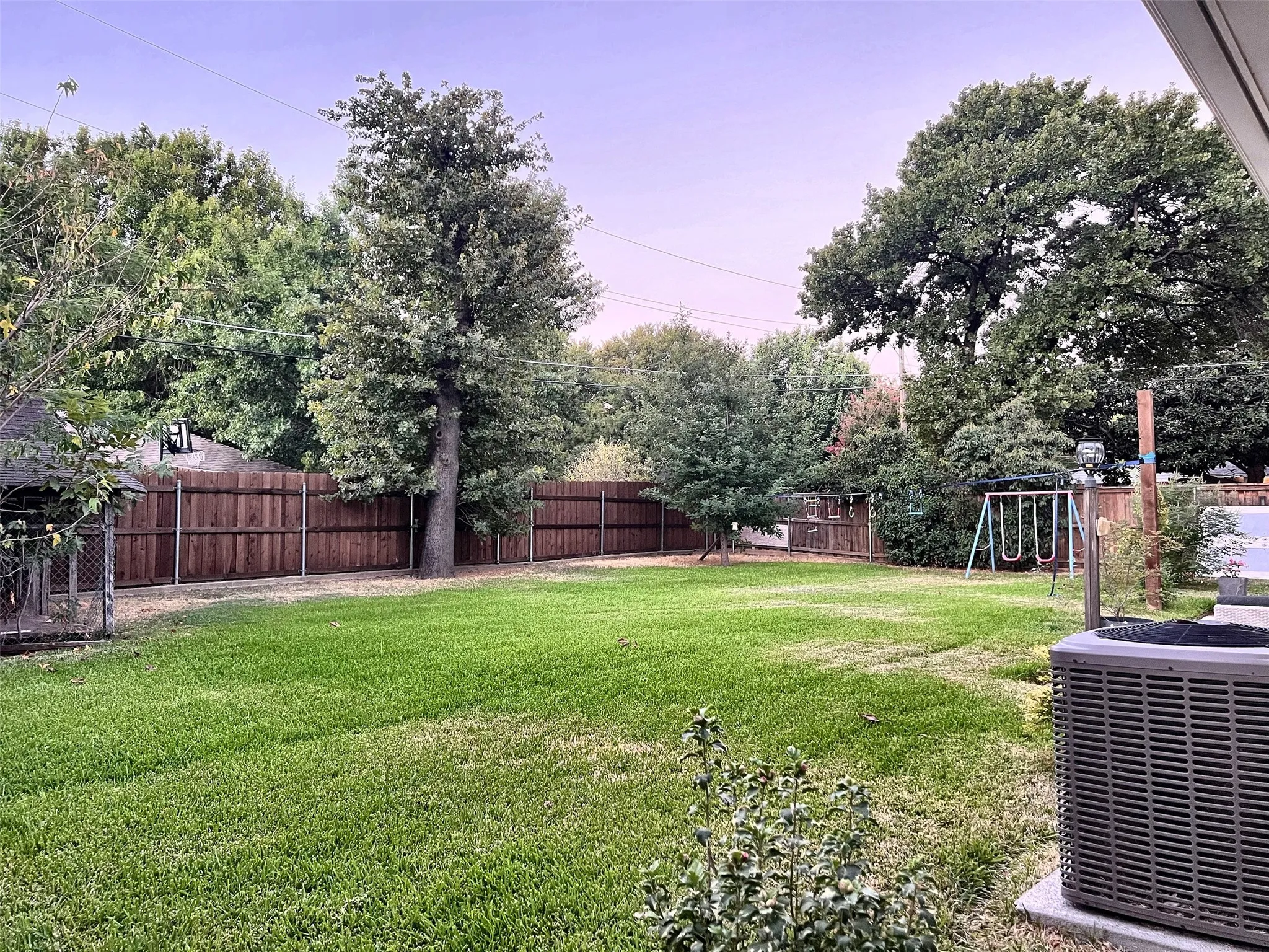 Expansive backyard featuring a lush lawn, mature trees, and privacy fencing