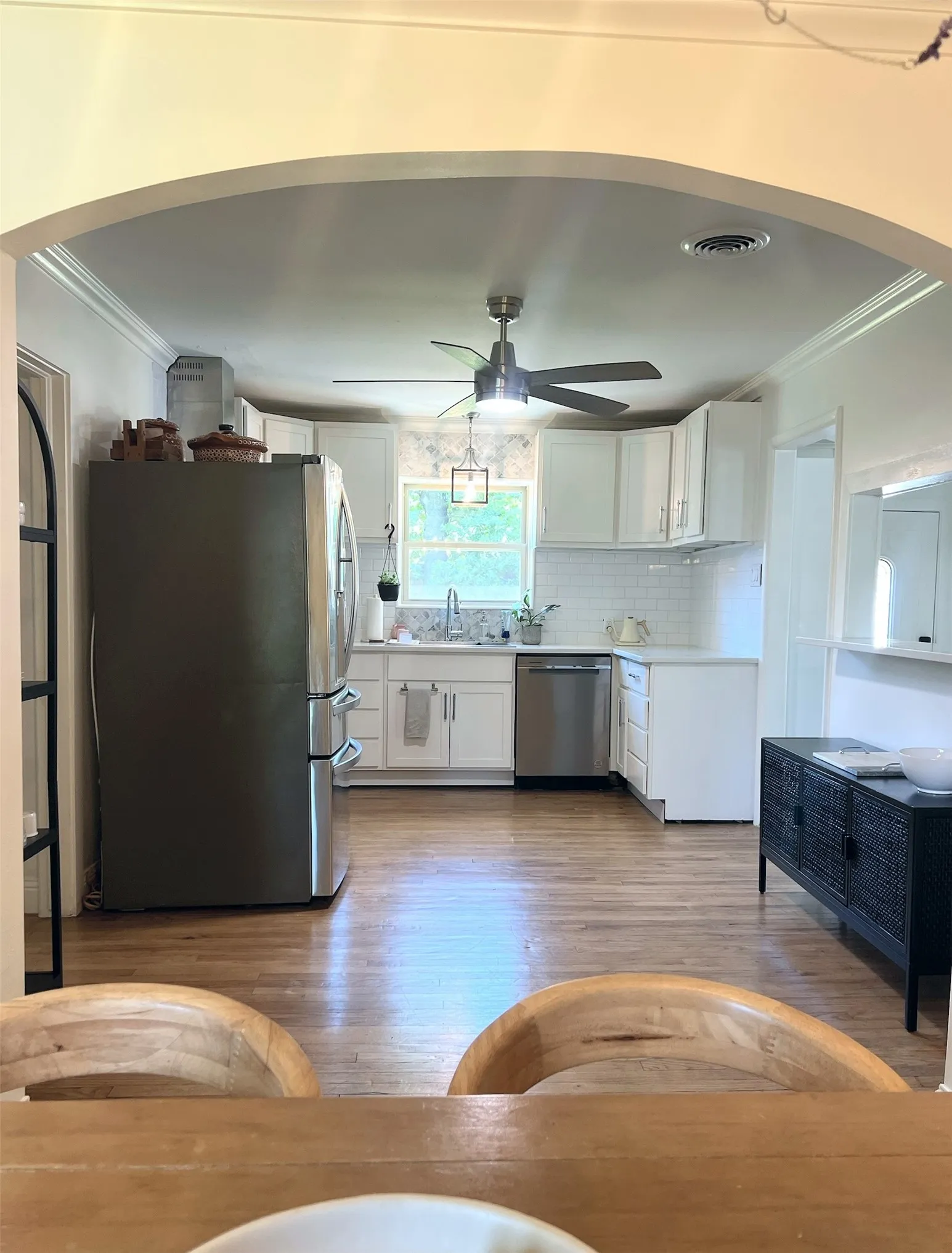 Archway entry to kitchen featuring wood-finish flooring, white cabinetry, stainless steel appliances, and subway tile backsplash