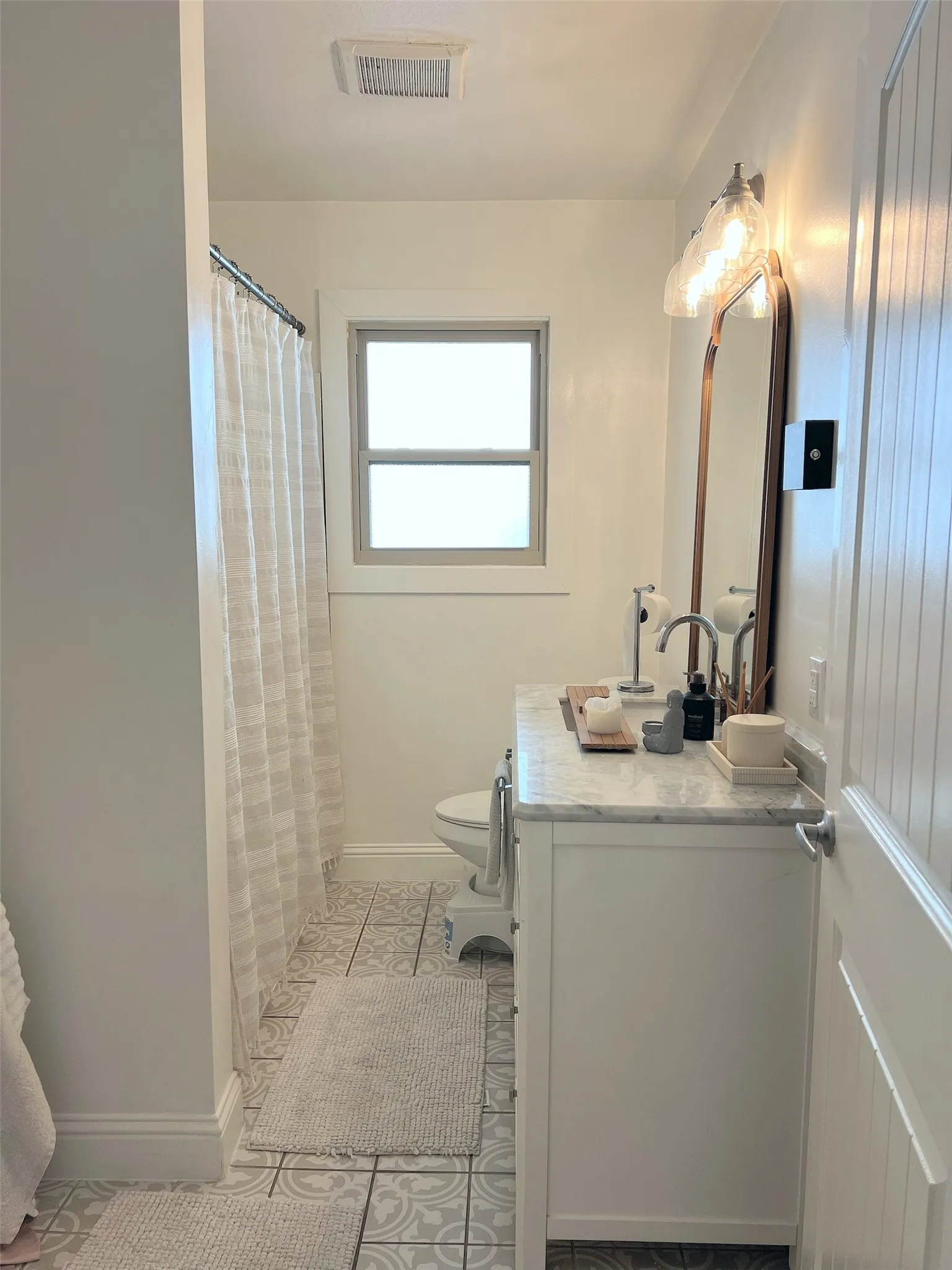 White single vanity with a marble-finish countertop, patterned floor tiling, and a window