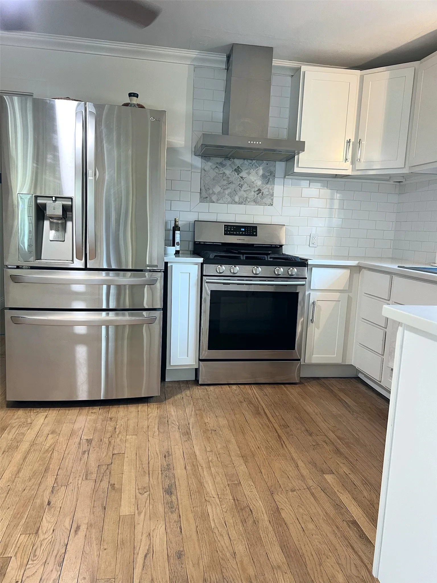 Stainless steel refrigerator, stainless steel range with hood, white cabinetry, subway tile backsplash, and wood-finish flooring