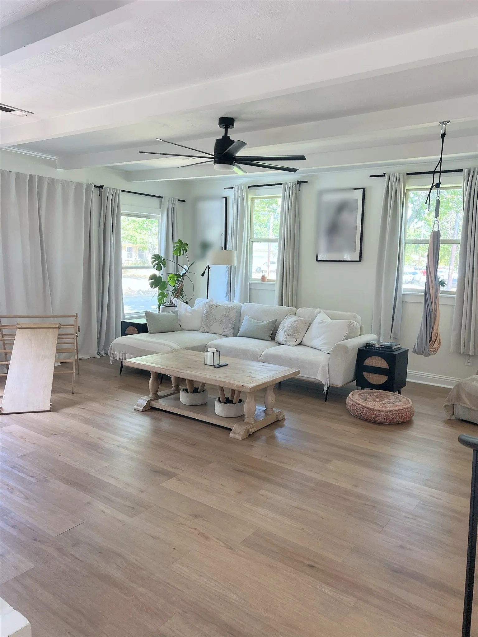 Wood-finish flooring throughout, complemented by a contemporary black ceiling fan and crisp white ceiling beams
