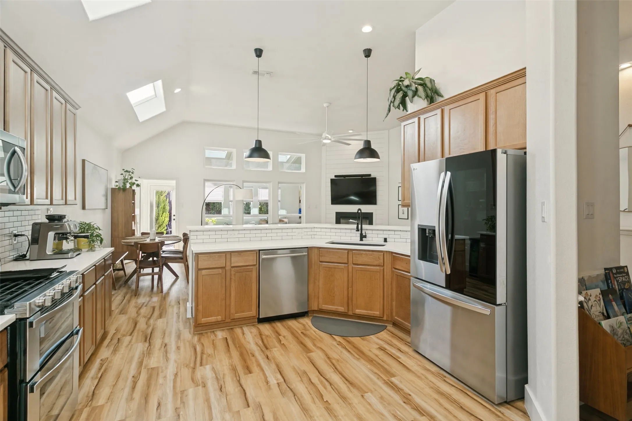 Vaulted ceiling with skylights, wood-finish flooring, stainless steel appliances, light wood cabinetry, and a subway tile backsplash