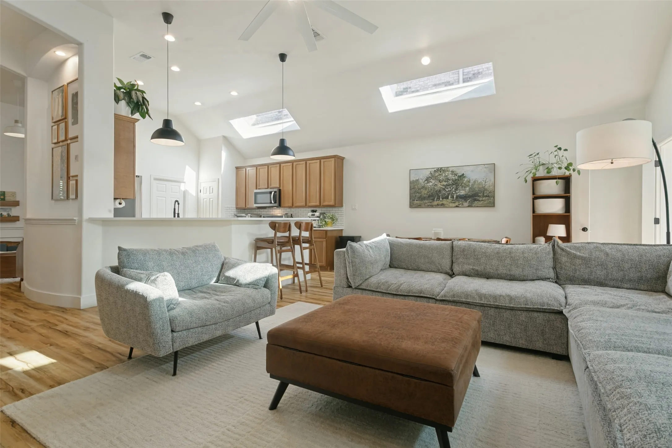 Vaulted ceiling with skylights, wood-finish flooring, recessed lighting, white walls, and a built-in kitchen peninsula
