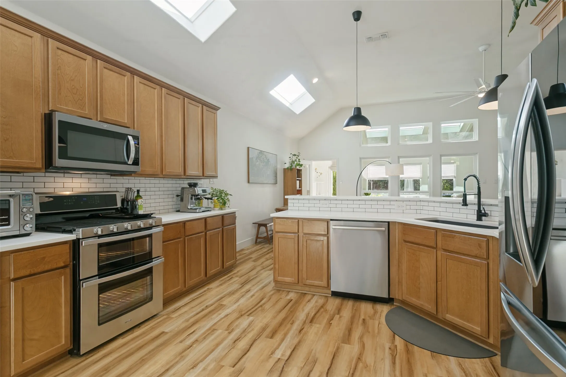 Kitchen with wood-finish flooring, light wood cabinetry, stainless steel appliances, and white subway tile backsplash