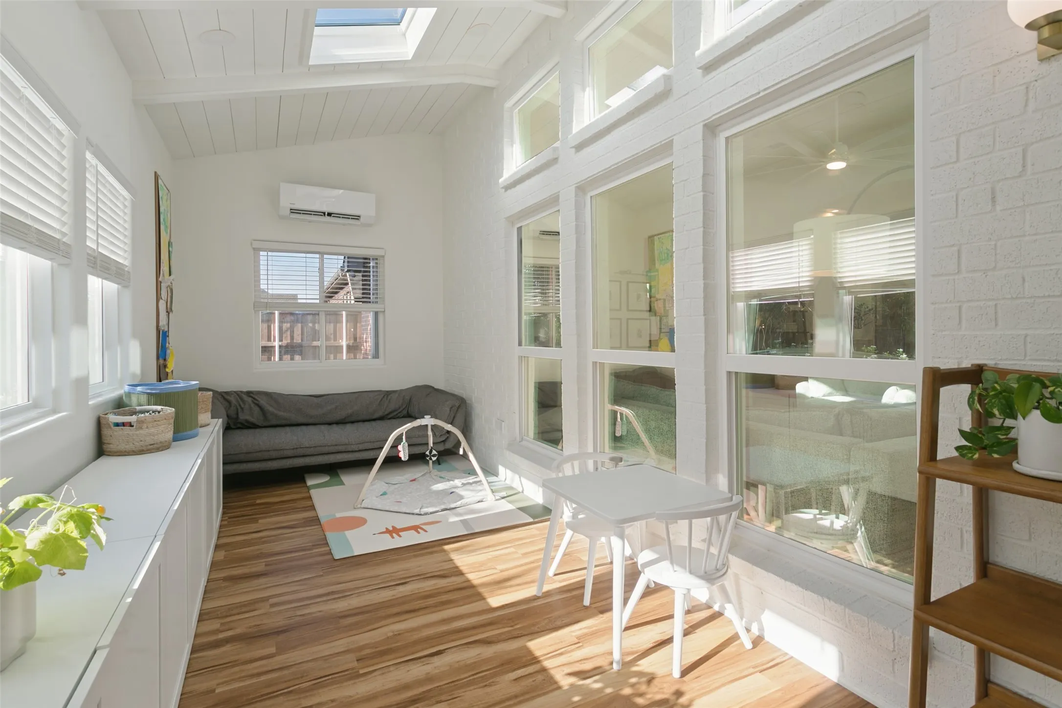 Vaulted ceiling with skylight, wood-finish flooring, white brick-finish wall, multiple large windows, and built-in cabinetry