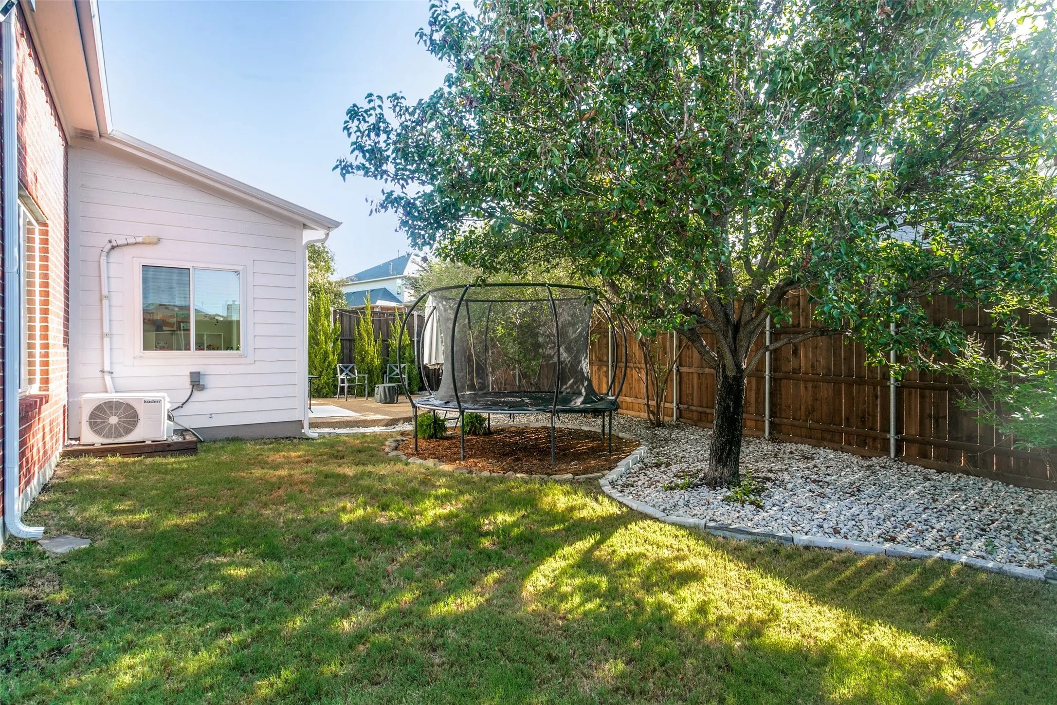 Expansive green lawn with mature tree, surrounded by rock and mulch landscaping, and a wood privacy fence
