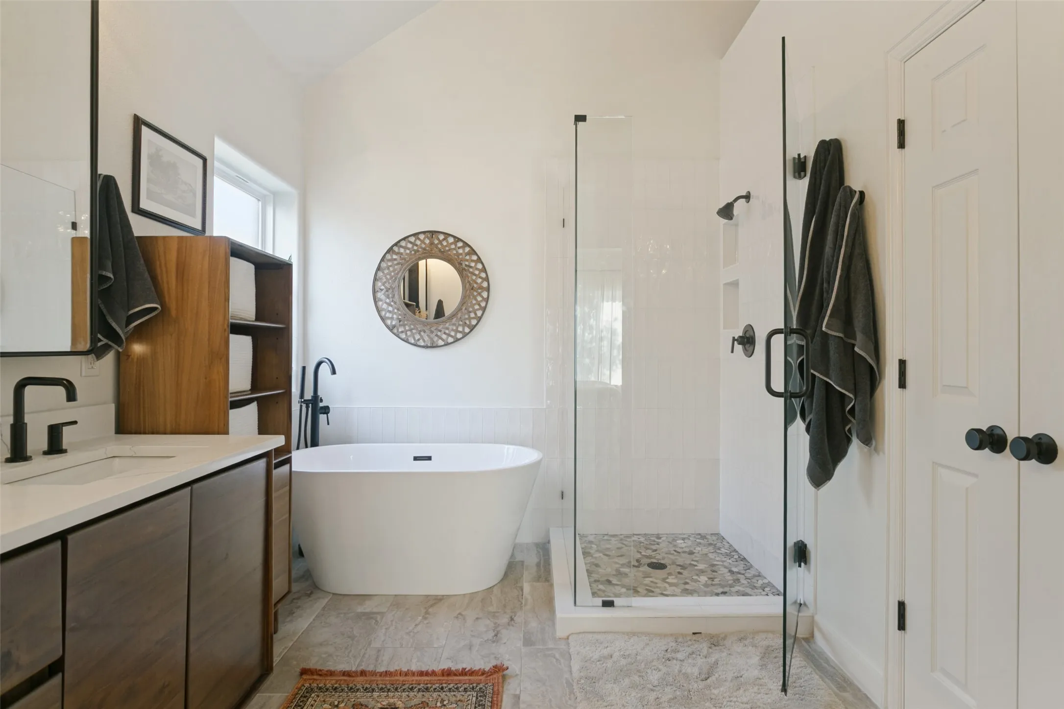 Freestanding soaking tub, walk-in shower with stone flooring, dual-basin vanity with wood-finish cabinetry, and matte black hardware