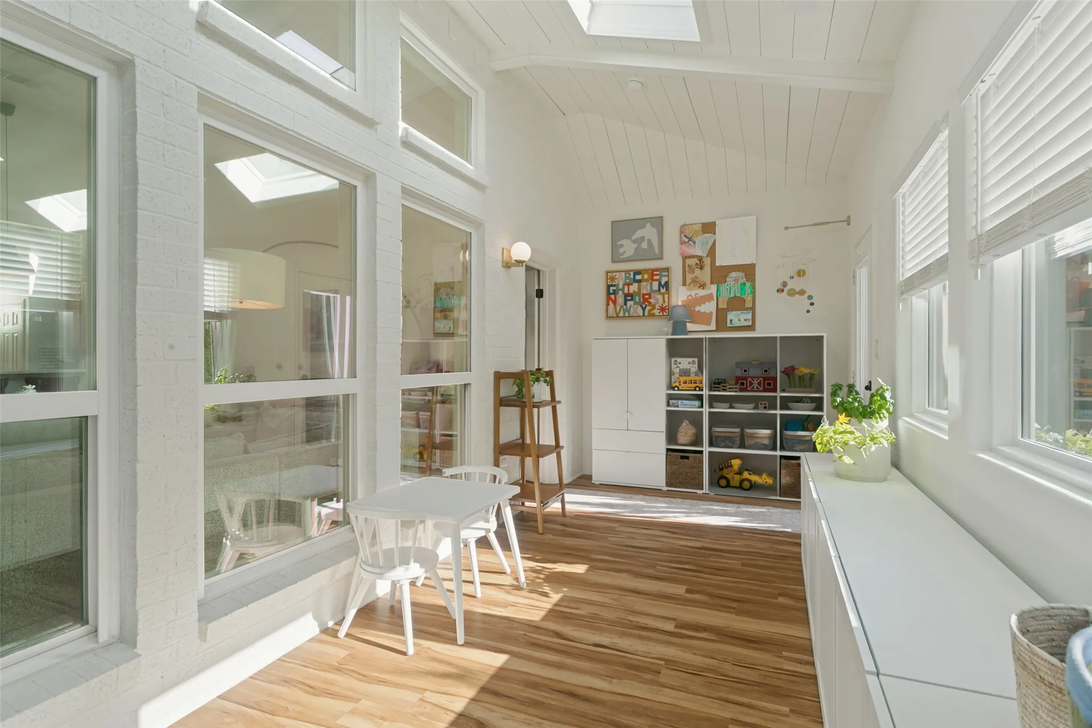 Vaulted plank ceiling, skylights, expansive wall of windows, white brick interior wall, and wood-finish flooring