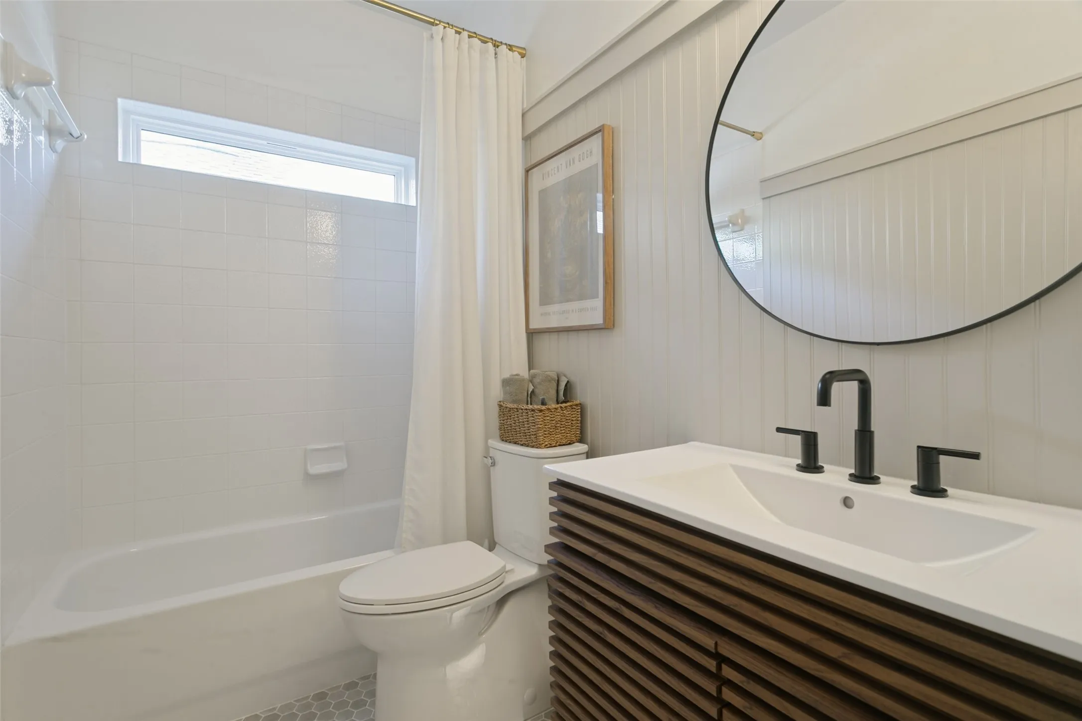 Contemporary vanity with integrated sink and matte black hardware, white subway tile shower surround, and a circular mirror