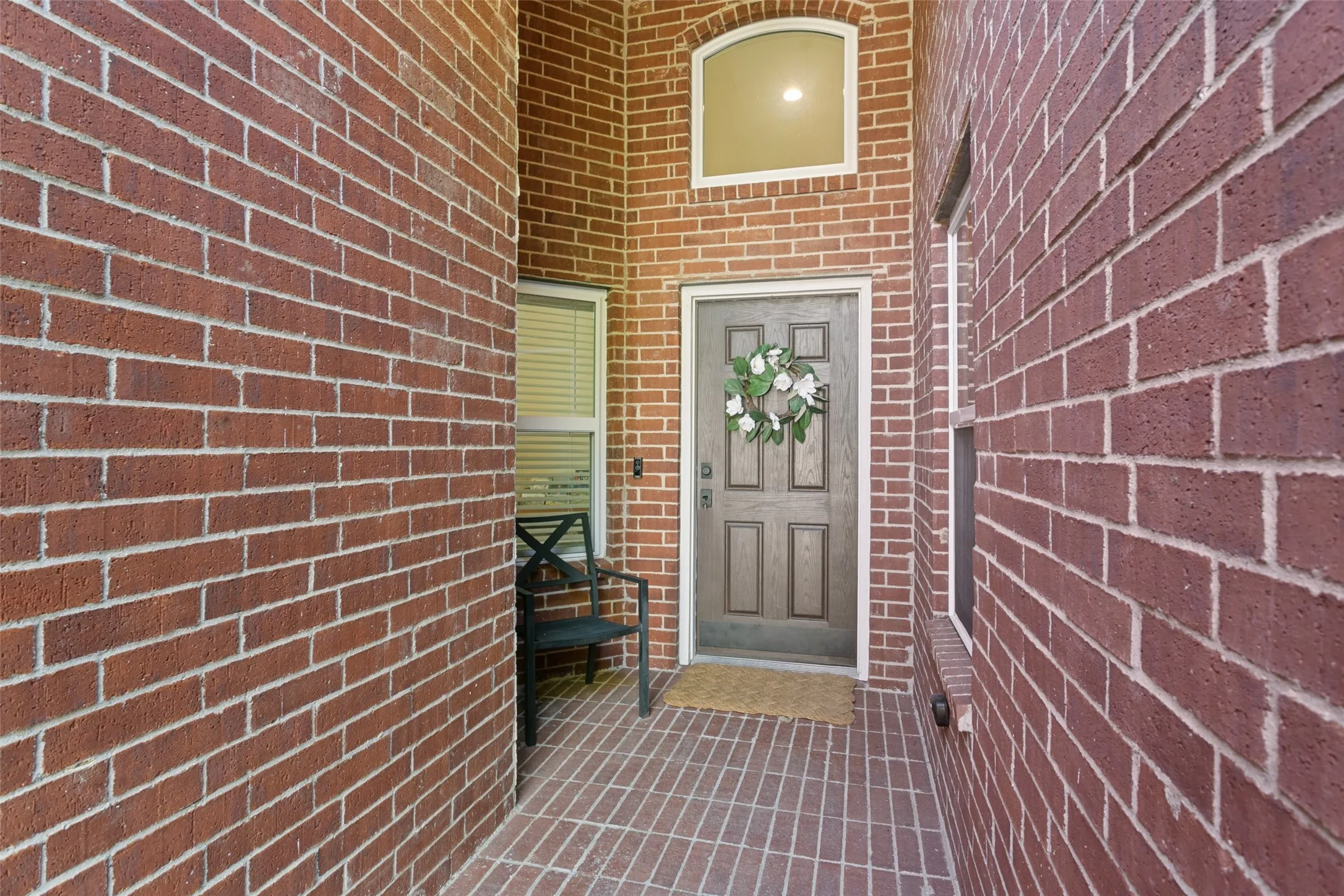 Brick exterior with a paneled entry door, arched transom window, and brick-patterned flooring at the entry