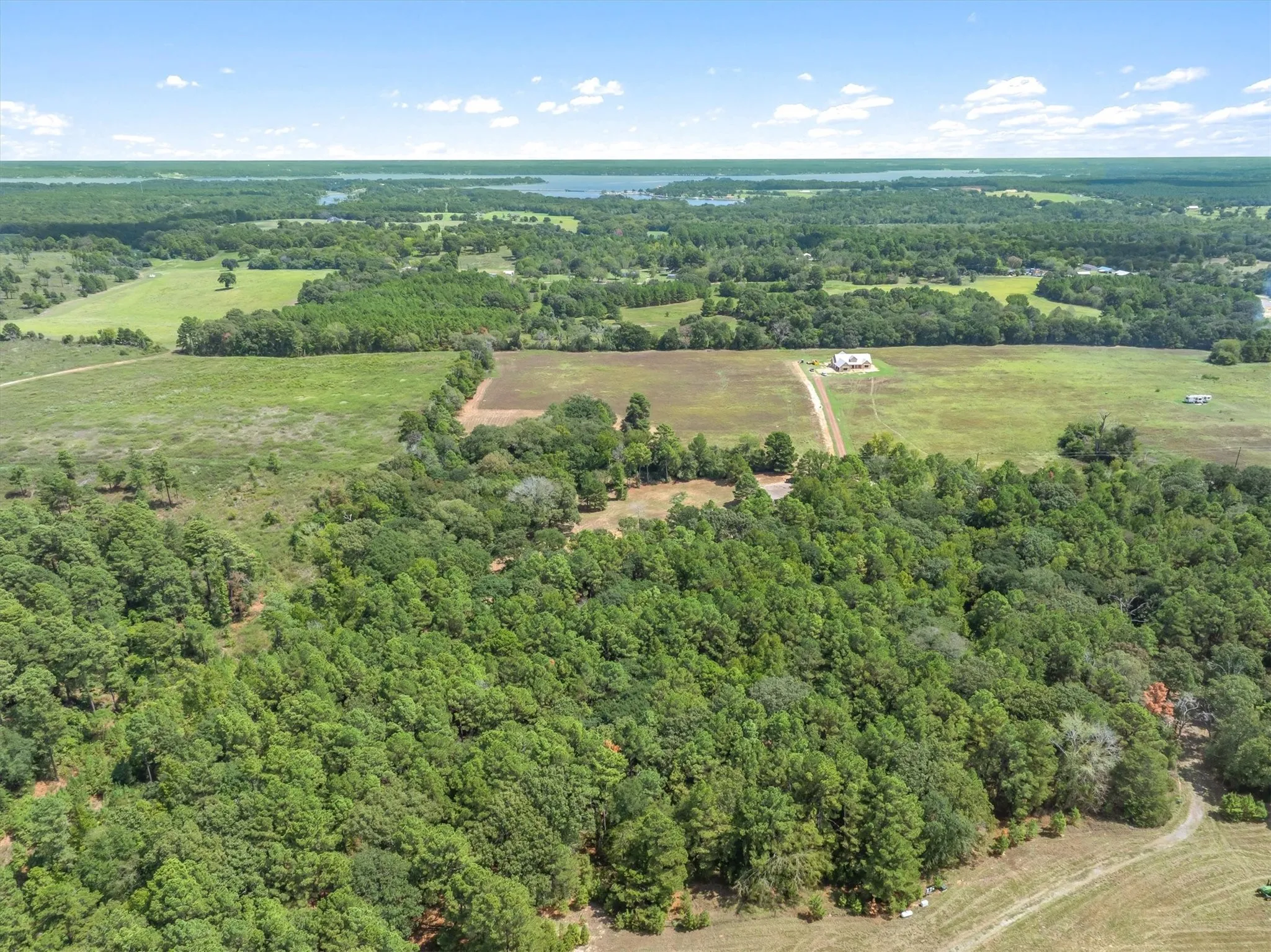 Expansive rural property featuring extensive tree coverage, open fields, and distant water bodies