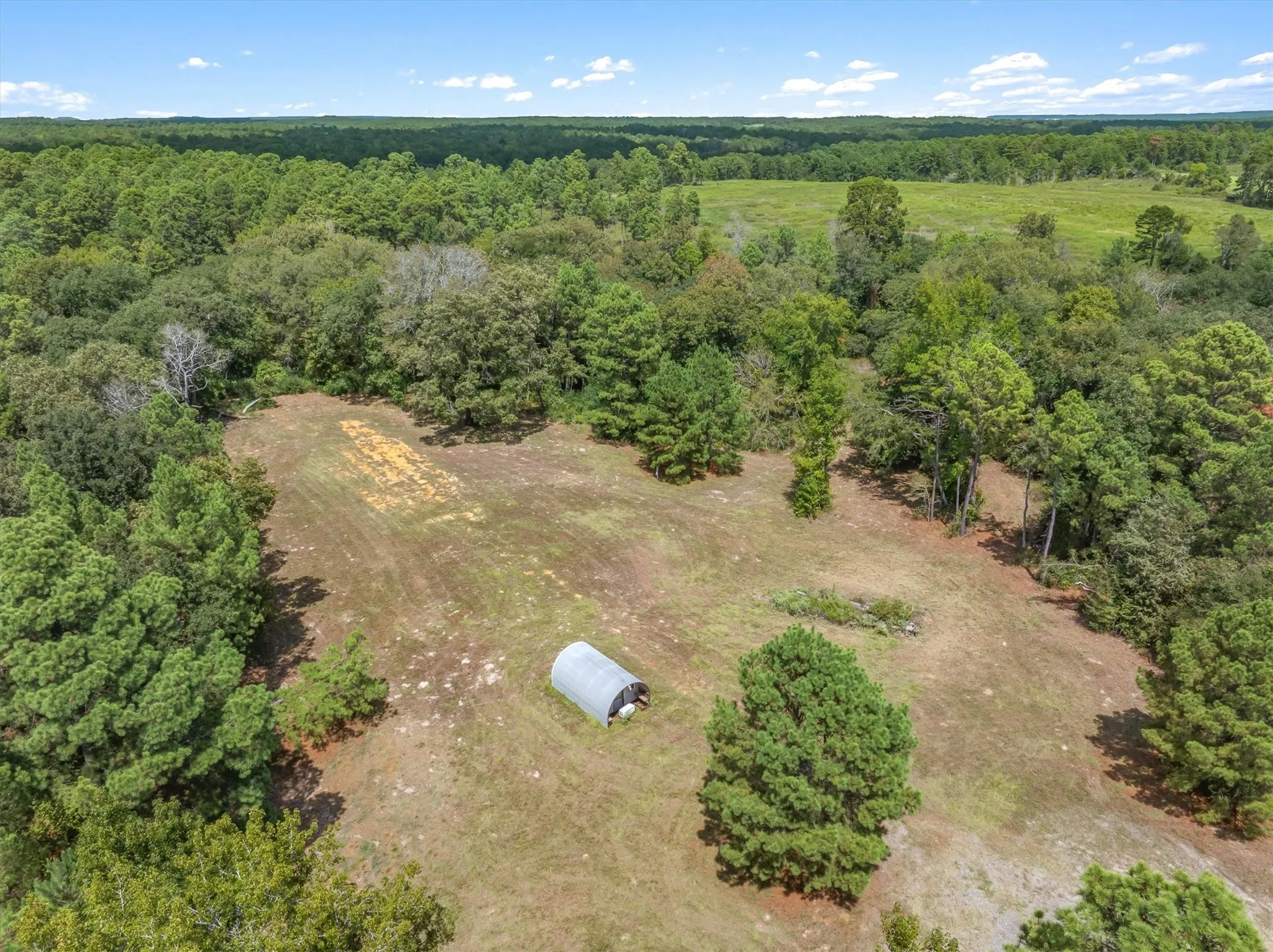 Expansive cleared land parcel with surrounding mature trees and open fields