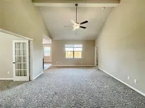 Vaulted ceilings with exposed beam, ceiling fan, neutral wall tones, window treatments, and French doors