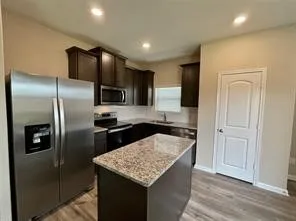 Kitchen featuring dark wood cabinetry, a central island with a speckled countertop, stainless steel appliances, and recessed lighting