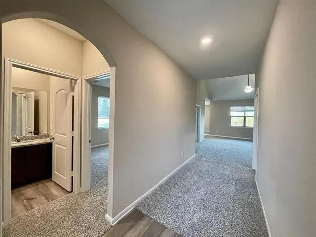 Arched doorway entry, recessed lighting, vaulted ceiling, wood-finish flooring, and a vanity with a stone countertop