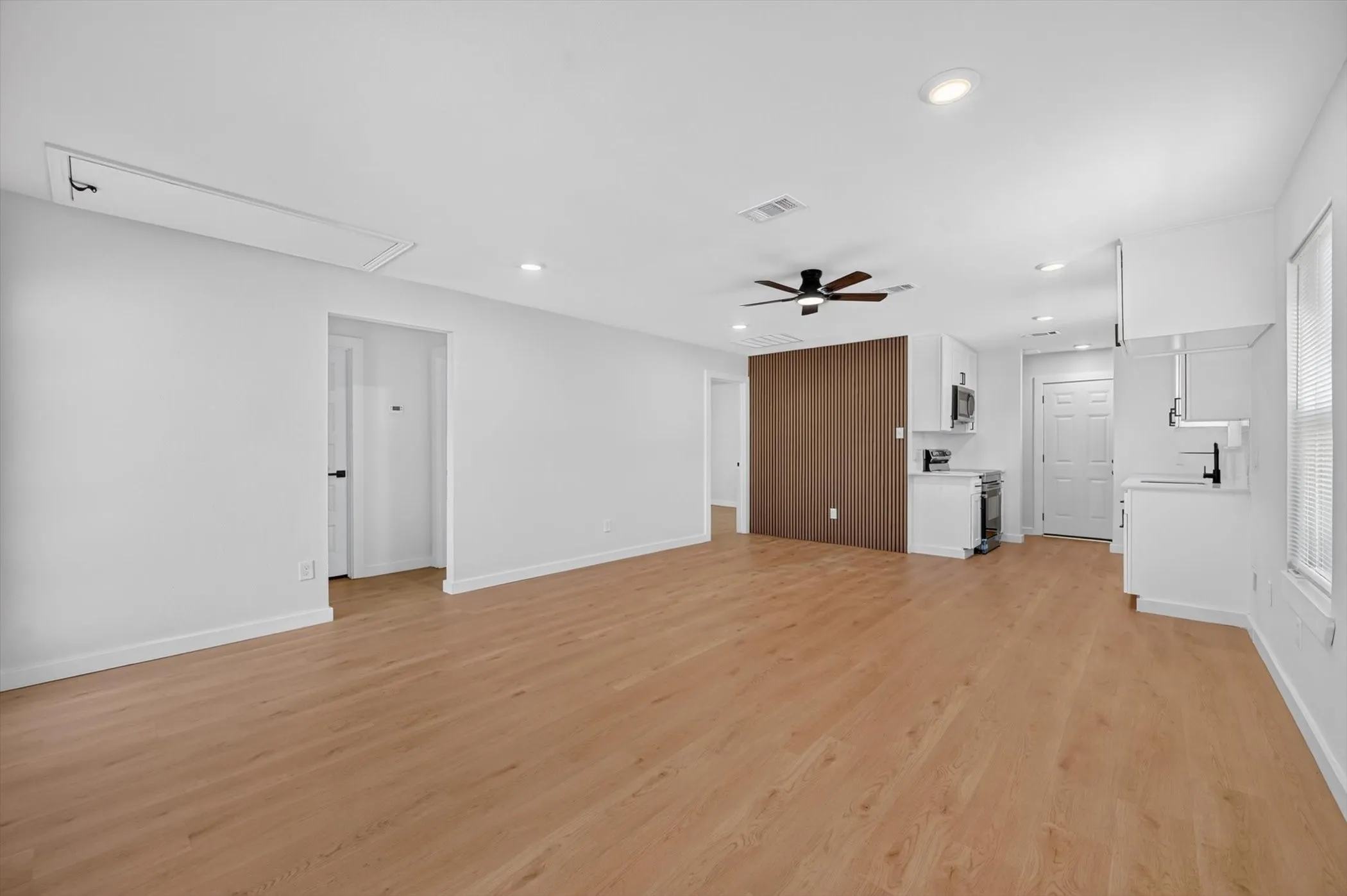 Open-concept living space with wood-finish flooring, recessed lighting, a ceiling fan, and a white kitchen featuring white cabinetry and stainless steel appliances