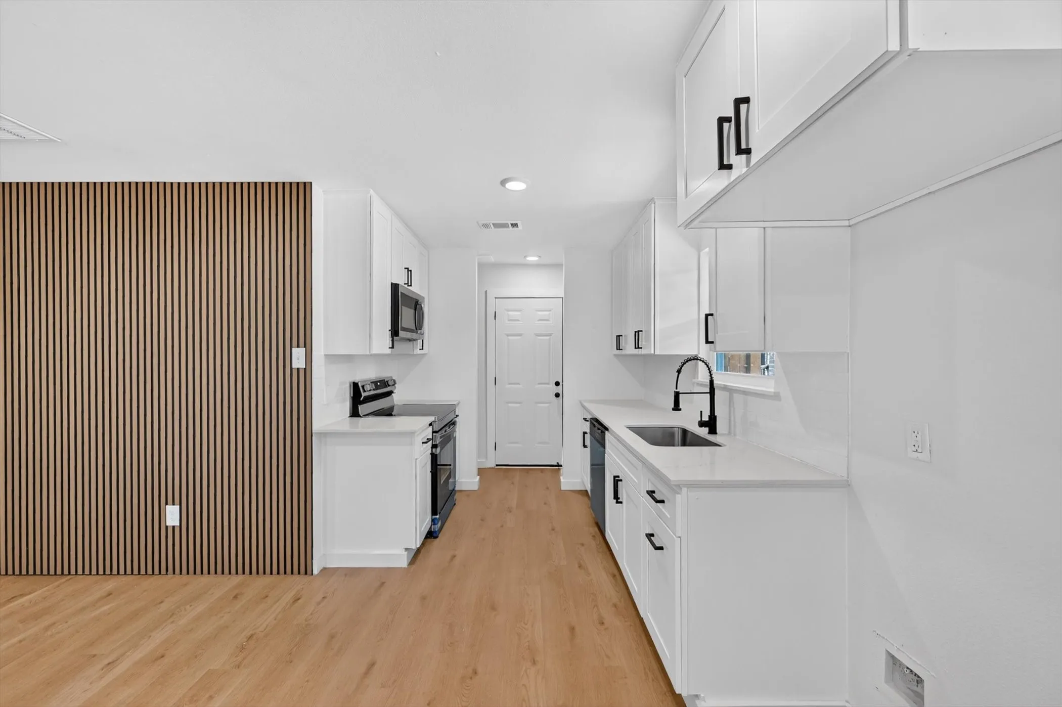 Updated kitchen featuring white shaker cabinetry, stainless steel appliances, quartz countertops, and matte black fixtures