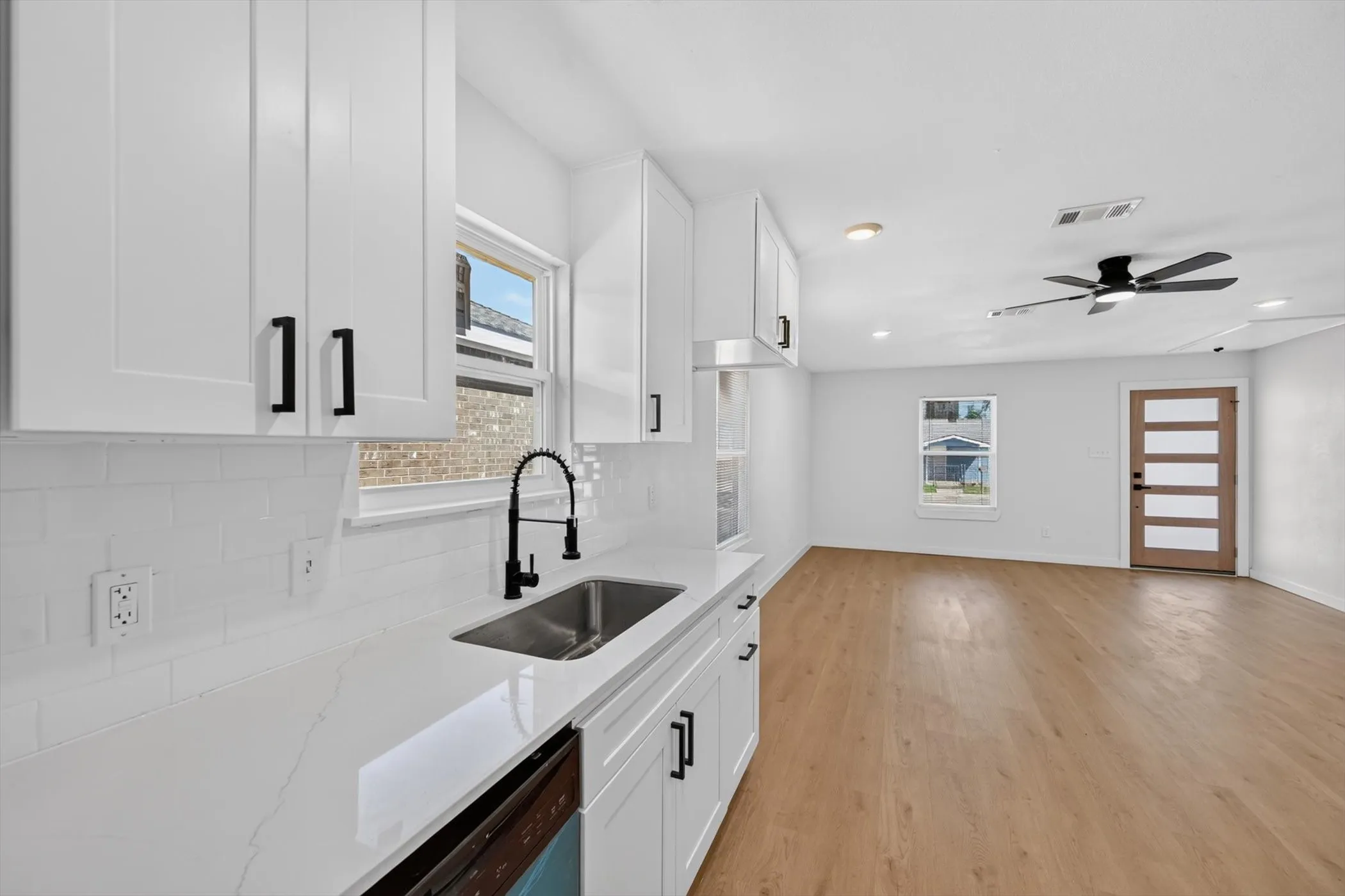 White shaker cabinetry with matte black hardware, stainless steel undermount sink with gooseneck faucet, light-toned wood-finish flooring, and a modern ceiling fan with integrated lighting