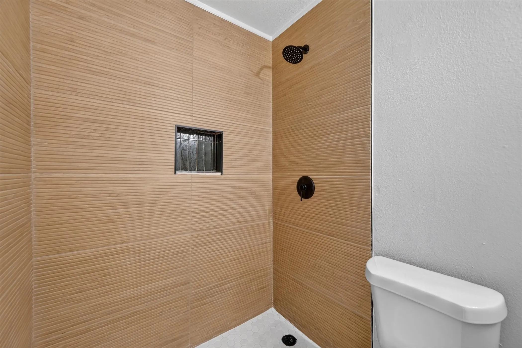 Textured shower surround with a built-in niche, matte black shower fixtures, and a white toilet