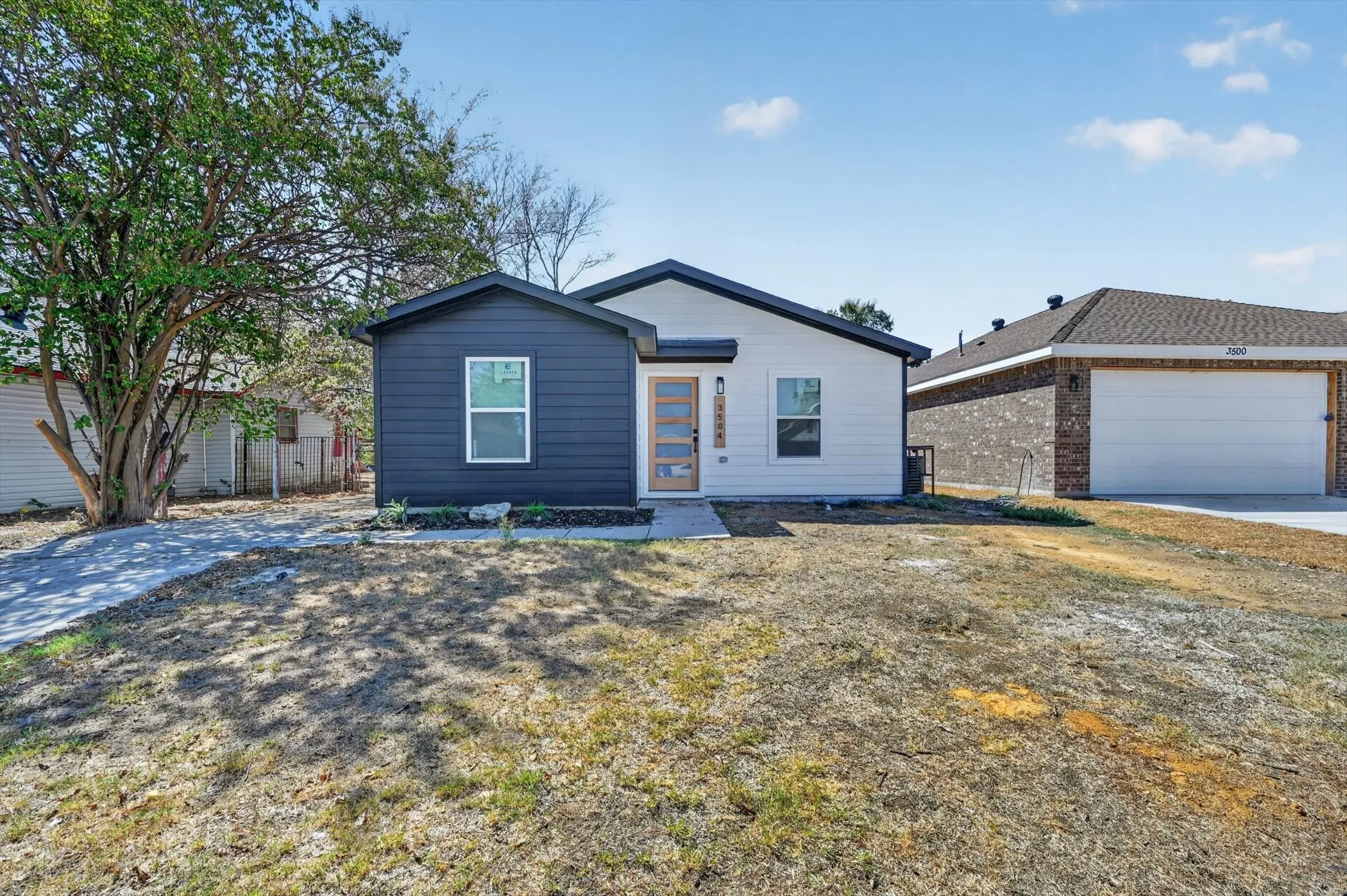 Contemporary exterior with white and dark siding, a light wood-finish front door, and a concrete walkway