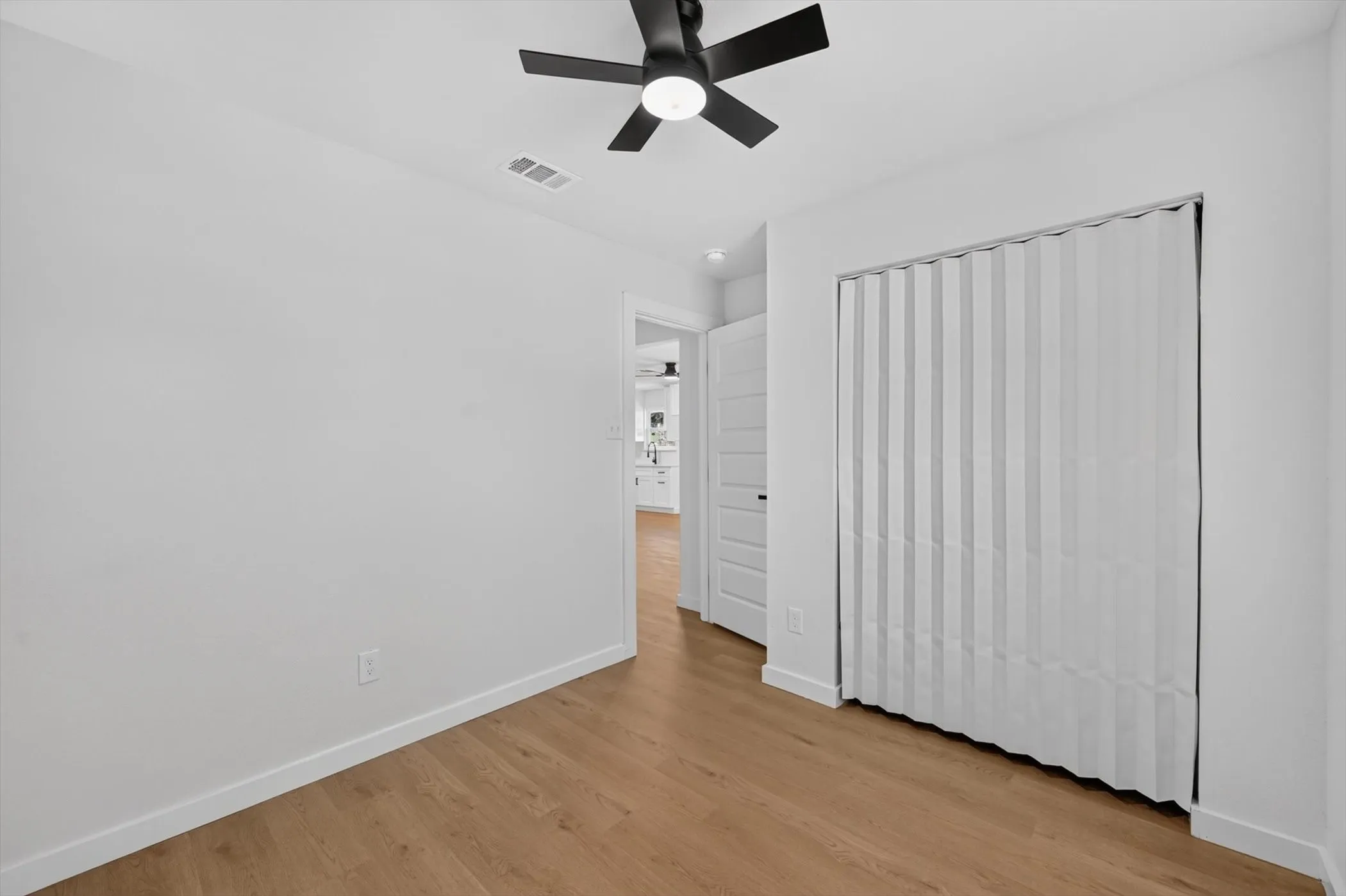 Wood-finish flooring, white walls, and a black ceiling fan with integrated lighting