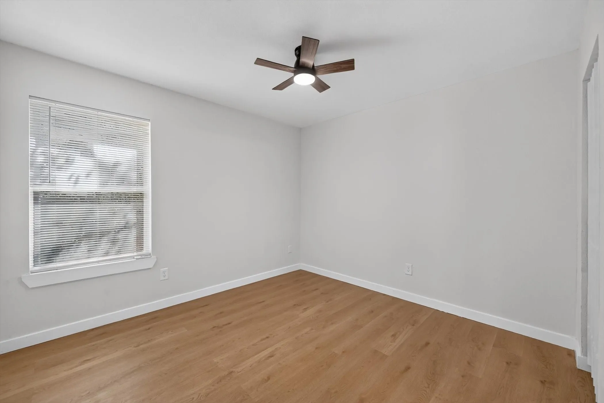 Wood-finish flooring, white walls, window with blinds, and a ceiling fan with integrated lighting