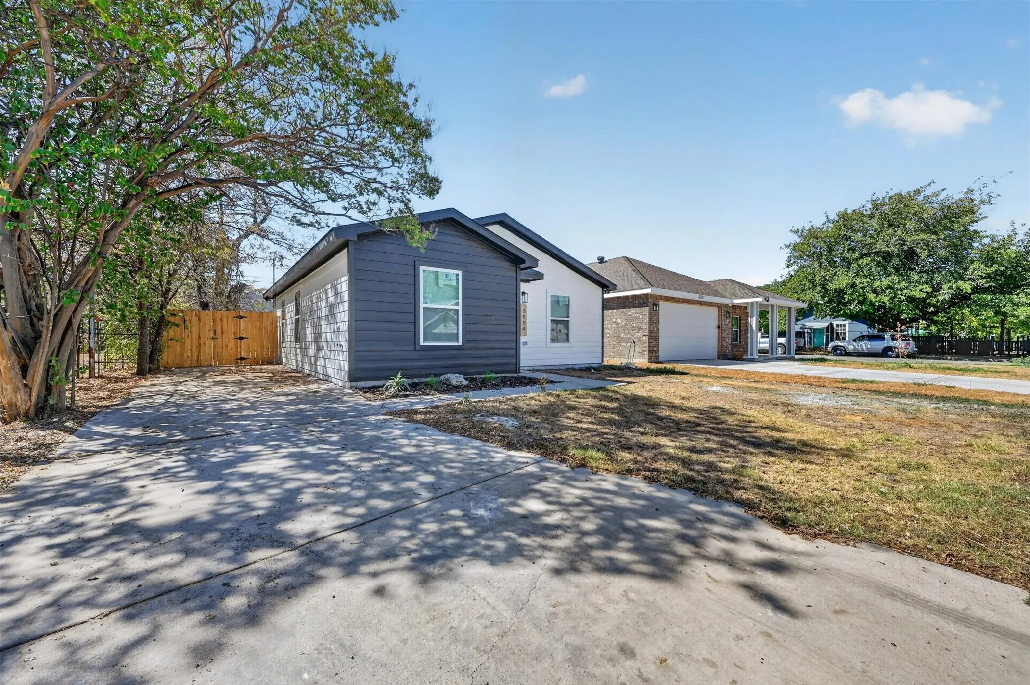 Paved driveway with tree coverage, dark gray horizontal siding, and a wood fence