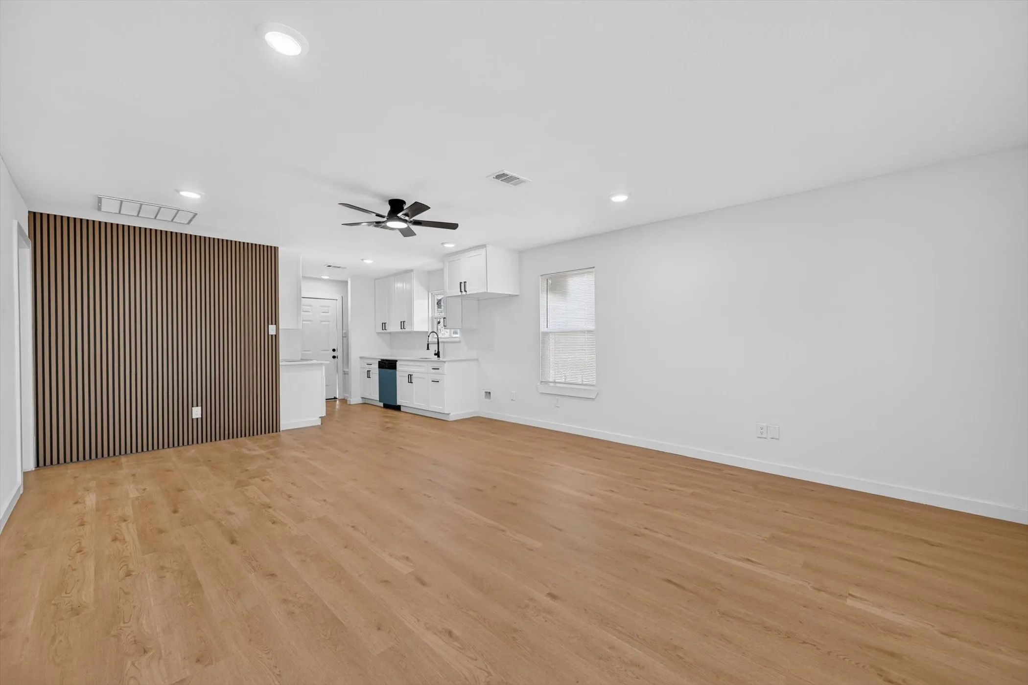 Open-concept living area with wood-finish flooring, recessed lighting, and a modern slatted accent wall