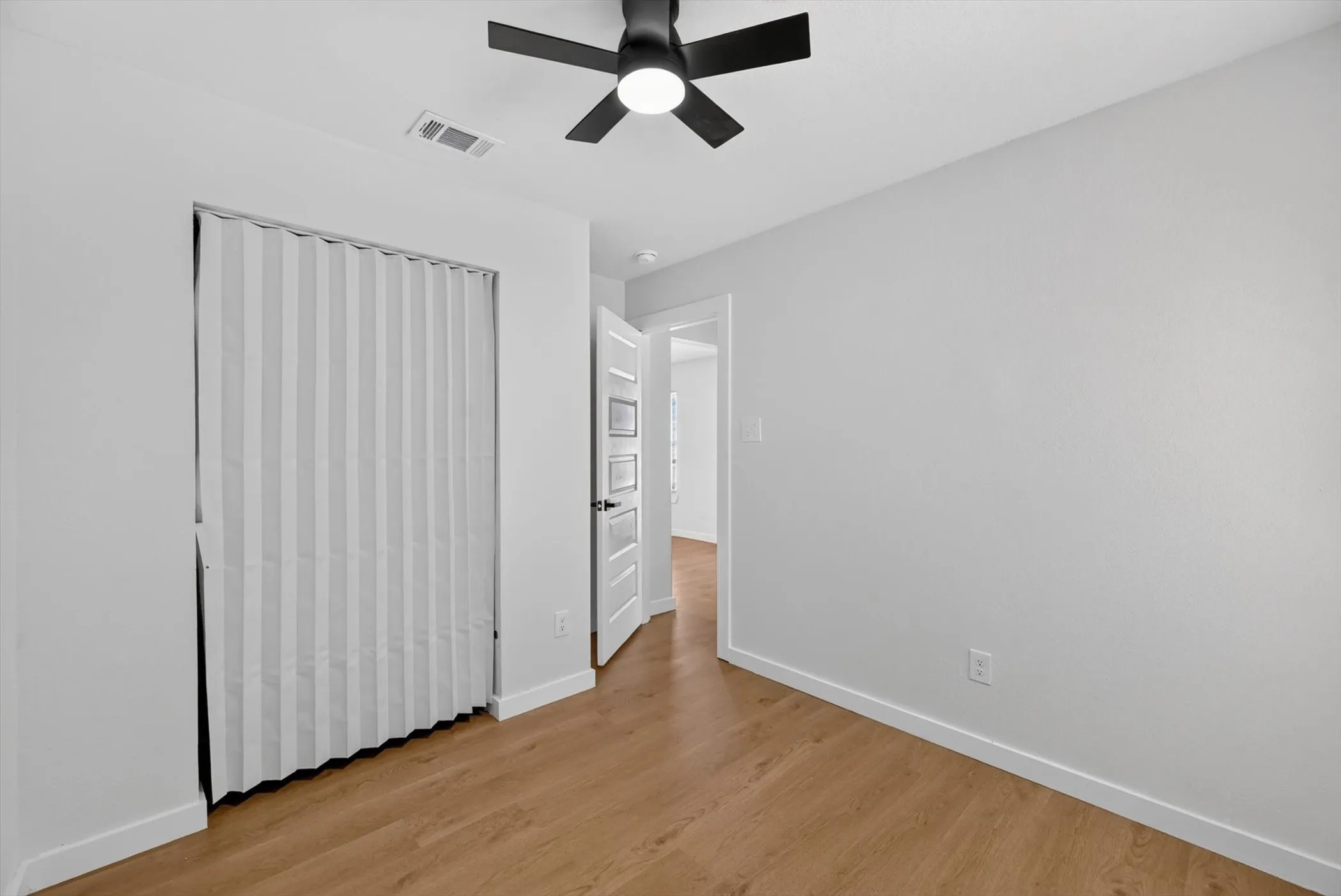 Wood-finish flooring, white walls, ceiling fan with integrated lighting, and a bi-fold closet door