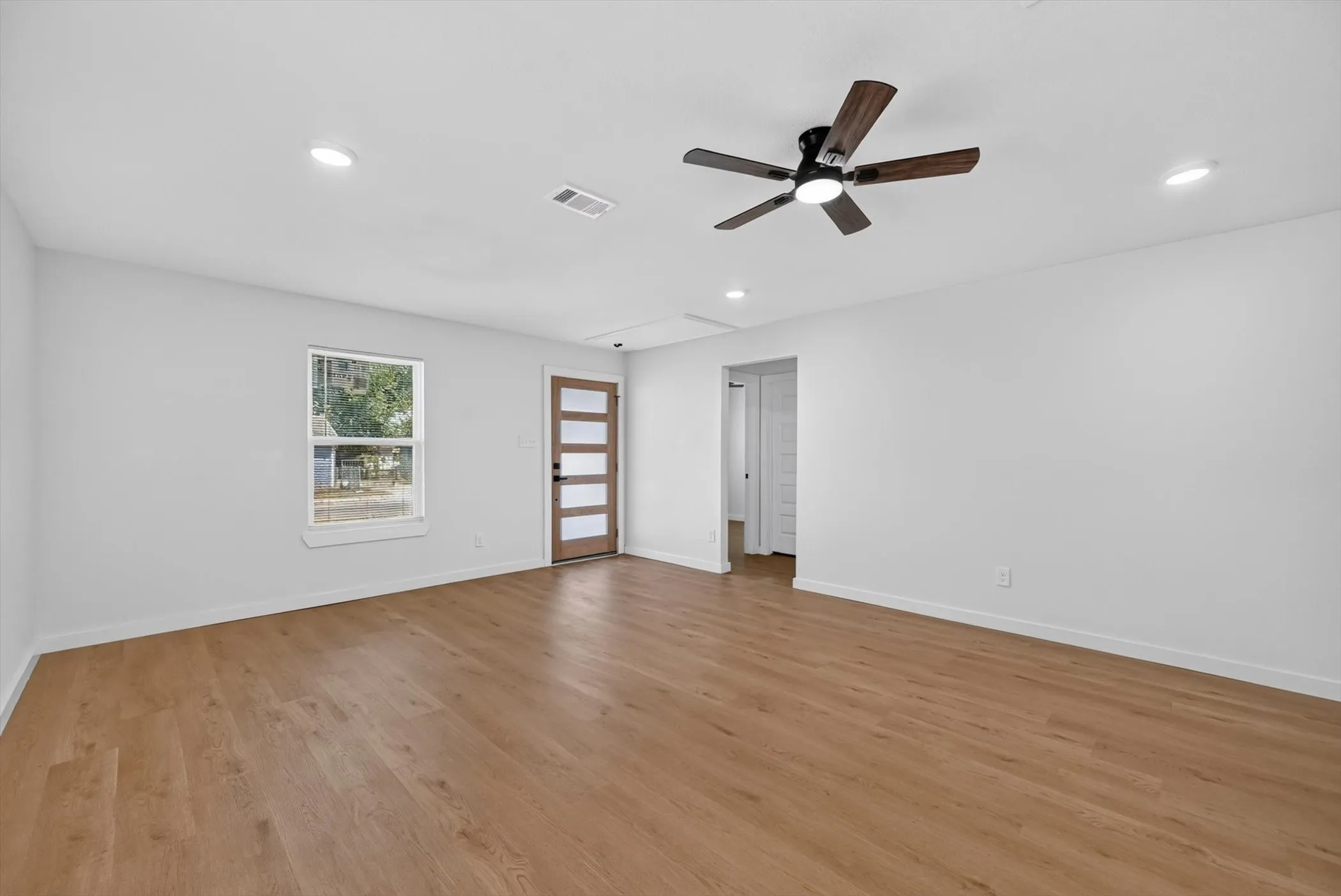 Spacious room featuring wood-finish flooring, a modern ceiling fan, recessed lighting, and a contemporary entry door with frosted glass panels