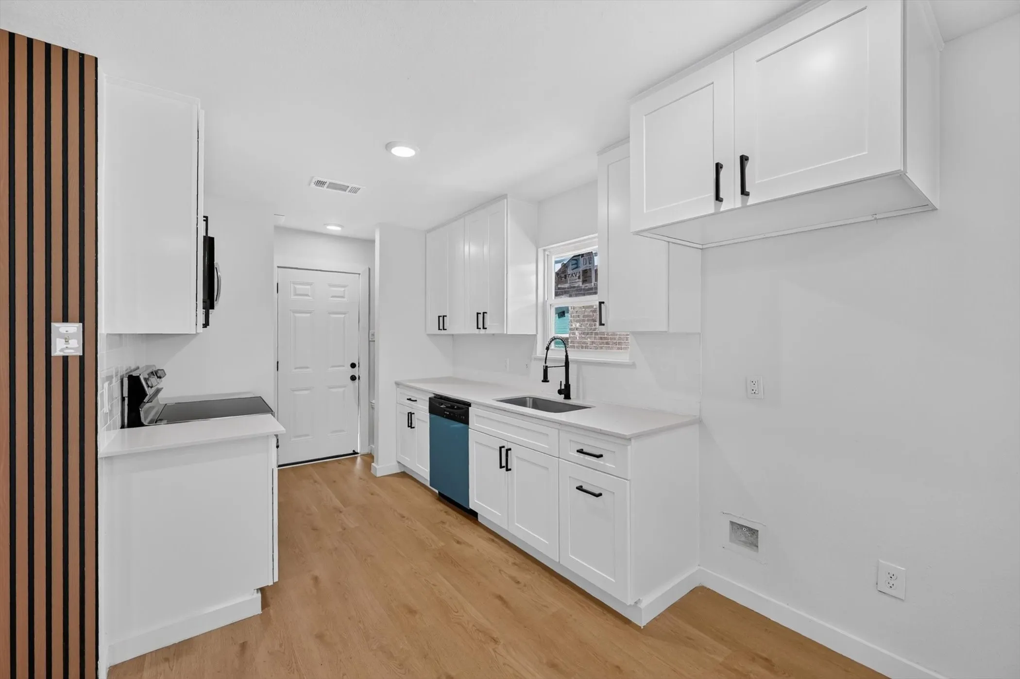 Kitchen featuring white cabinetry, light wood-finish flooring, quartz countertops, a stainless steel sink with a matte black faucet, and a paneled accent wall