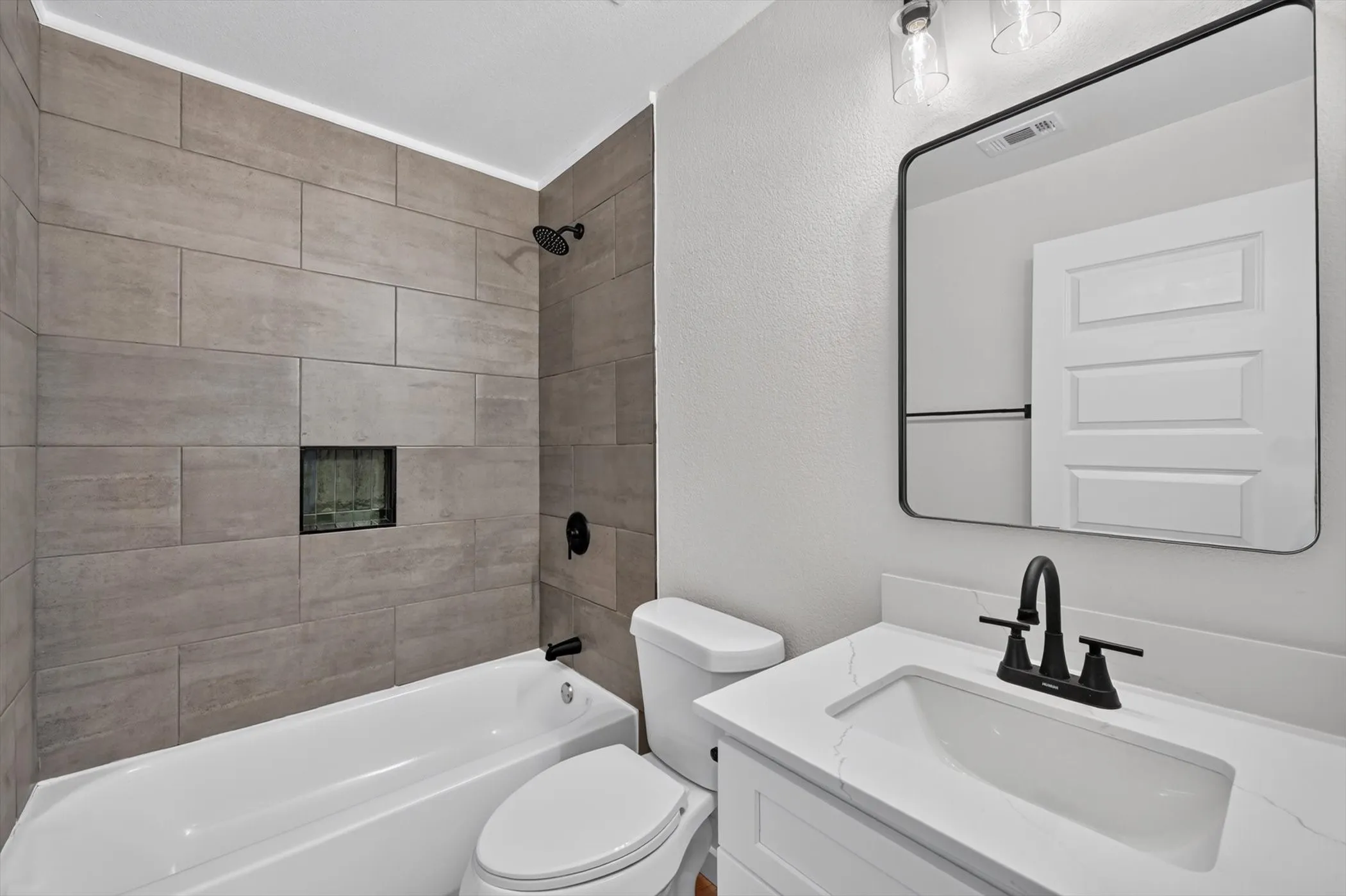 Bathroom featuring a white tub, tiled shower surround with built-in niche, vanity with white countertop, and a black-framed mirror