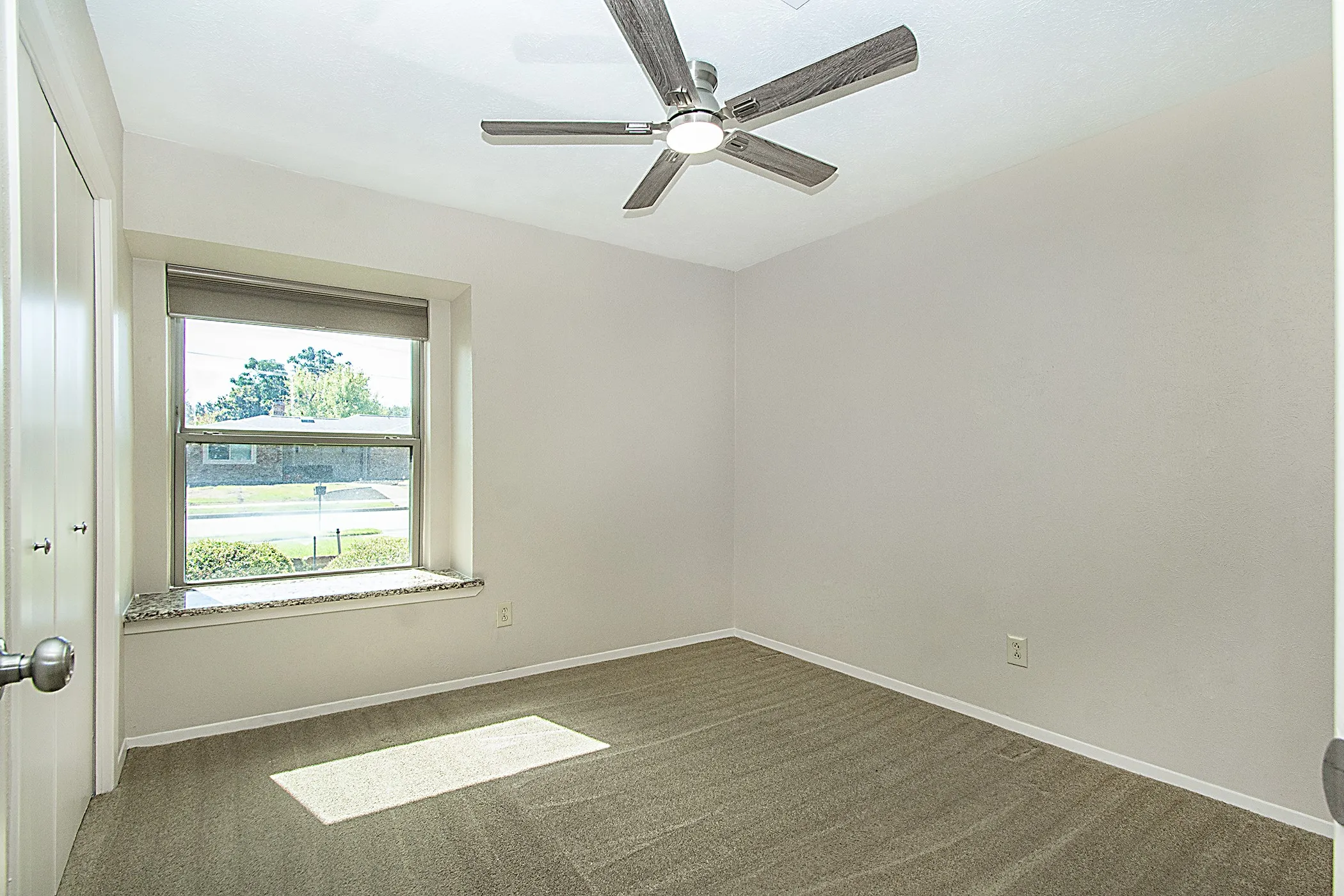 Neutral wall paint, carpet flooring, window with a stone-finish sill, and a ceiling fan with integrated lighting