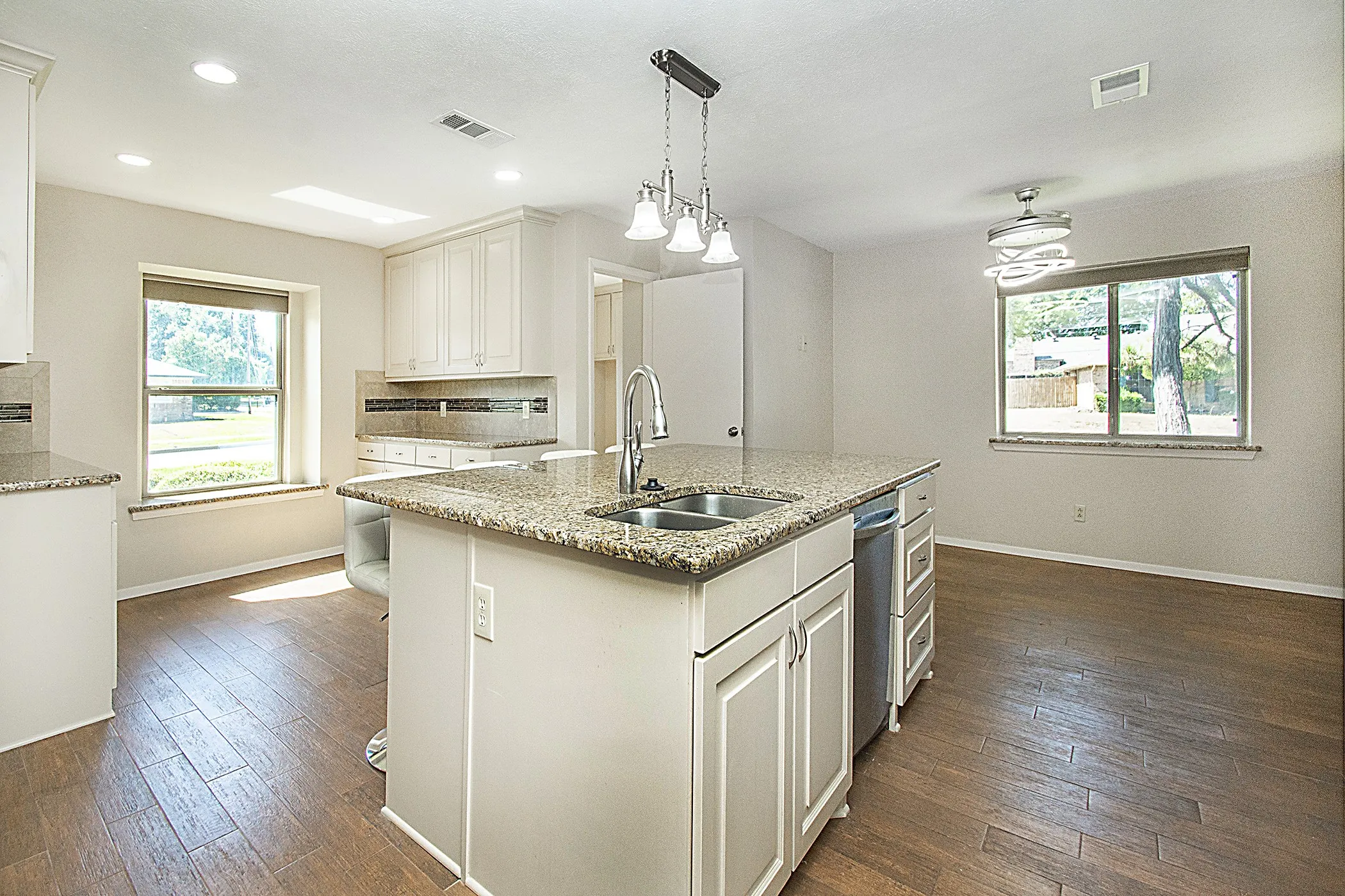 Kitchen featuring a large island with a double basin sink, granite countertops, white cabinetry, wood-finish flooring, and recessed lighting