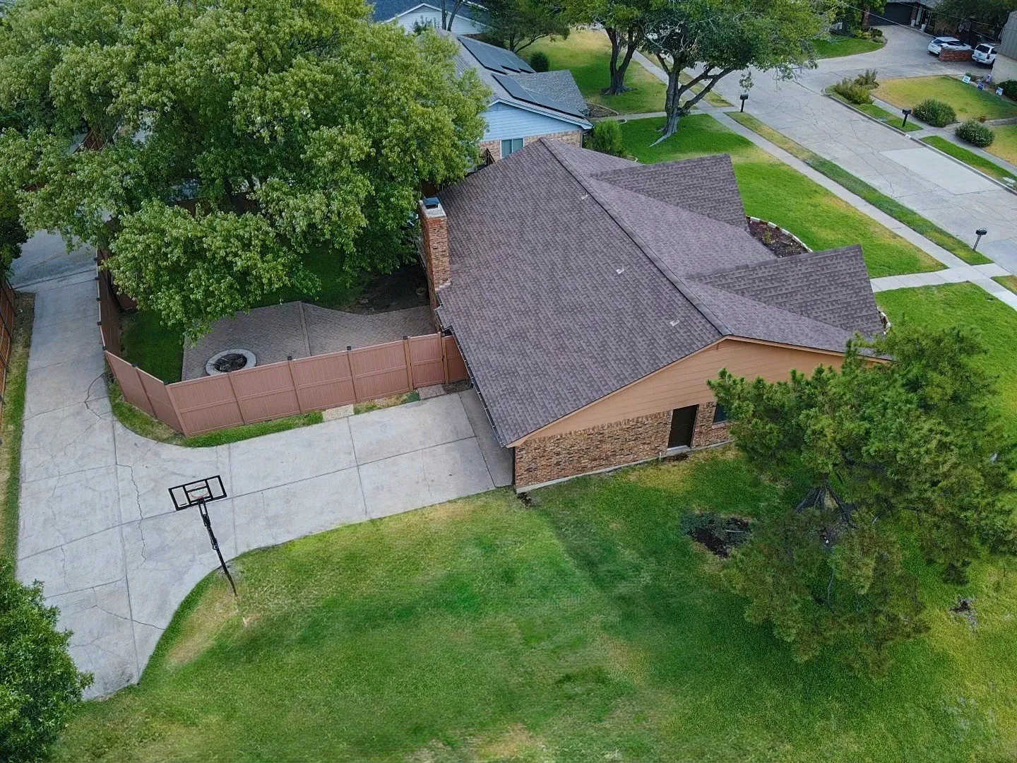 Expansive concrete driveway, mature trees, enclosed patio with fire pit, and a brick and siding exterior
