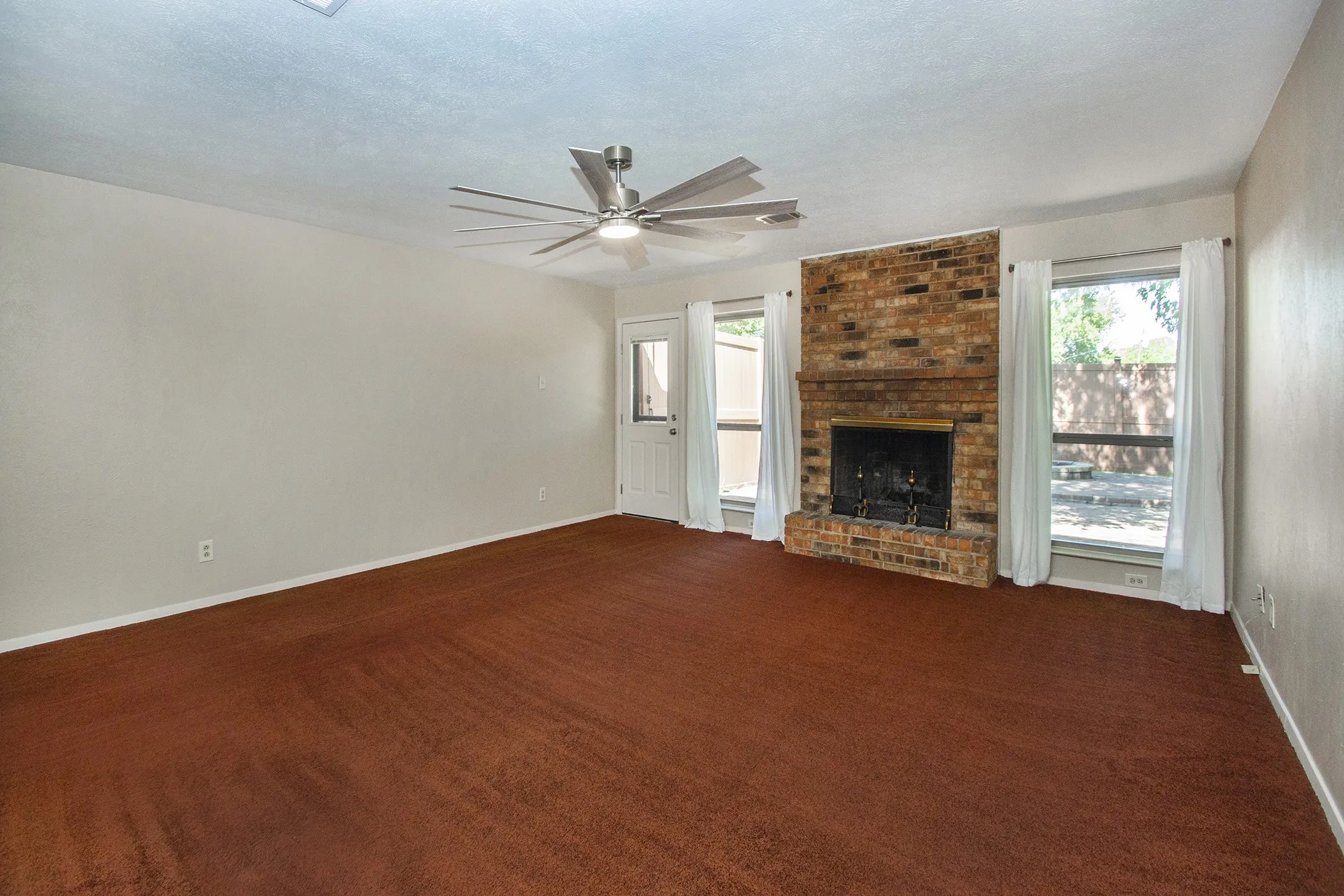 Brick fireplace with a metal grate, brushed nickel ceiling fan, white paneled door with glass insert, and two windows with white trim