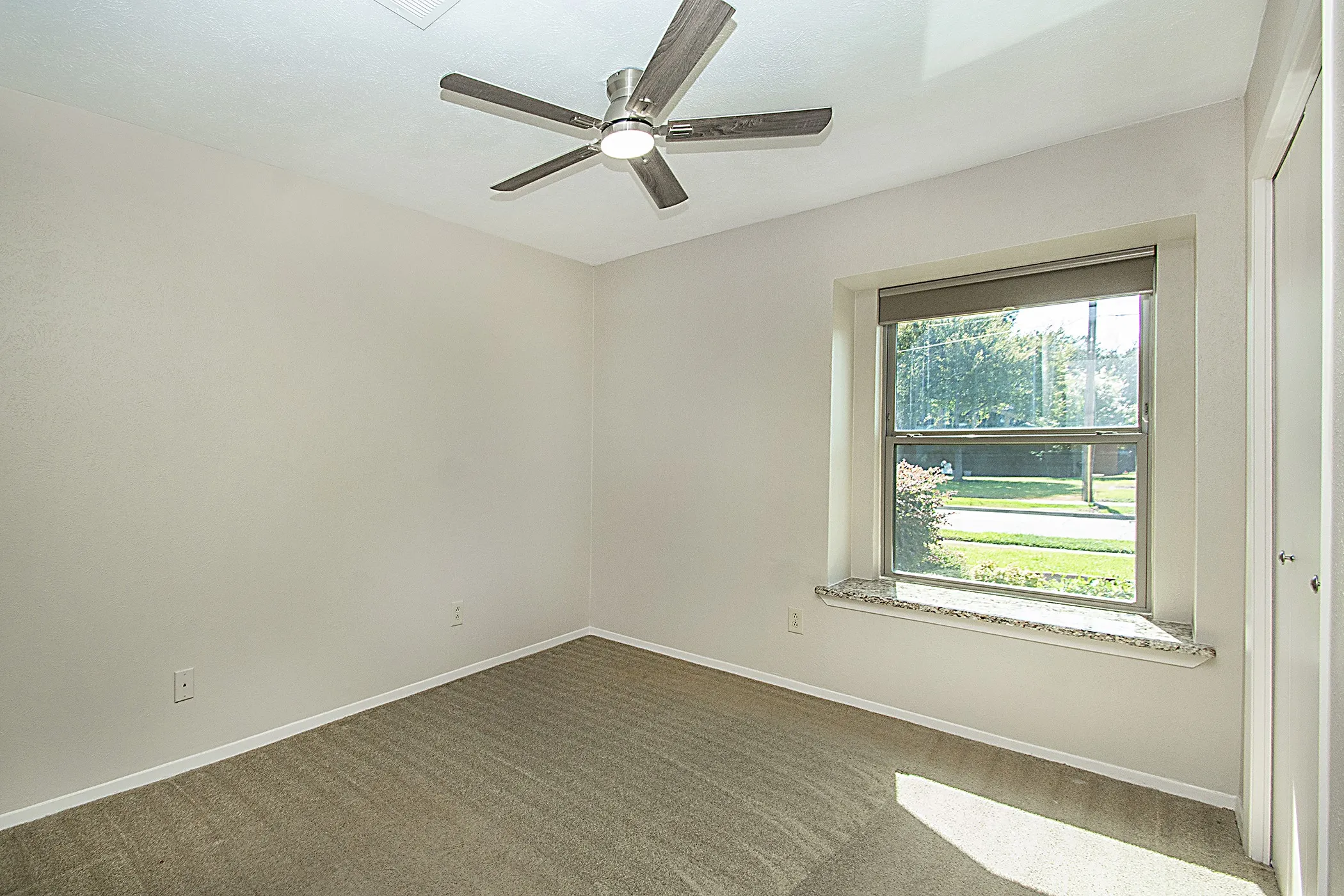 Neutral wall finishes, textured carpeting, a ceiling fan with integrated lighting, and a window with a stone-finish sill