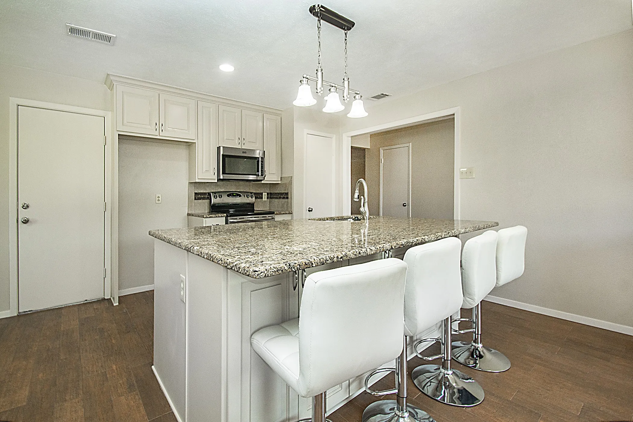 Kitchen featuring wood-finish flooring, granite island countertop, white cabinetry, stainless steel microwave, and a chrome faucet