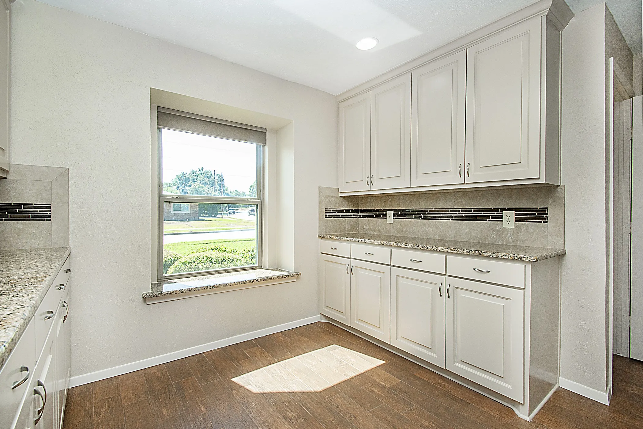 Wood-finish flooring, white cabinetry, granite countertops, tile backsplash, and recessed lighting