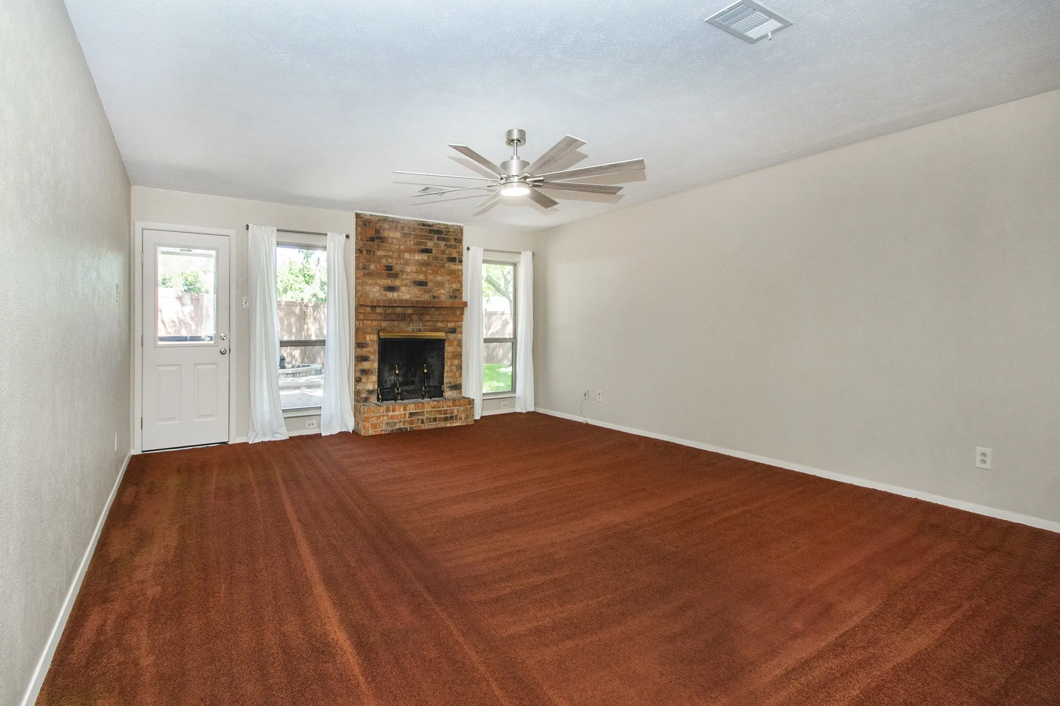 Spacious room featuring a brick-surround fireplace, multiple windows, a ceiling fan, and a door providing exterior access